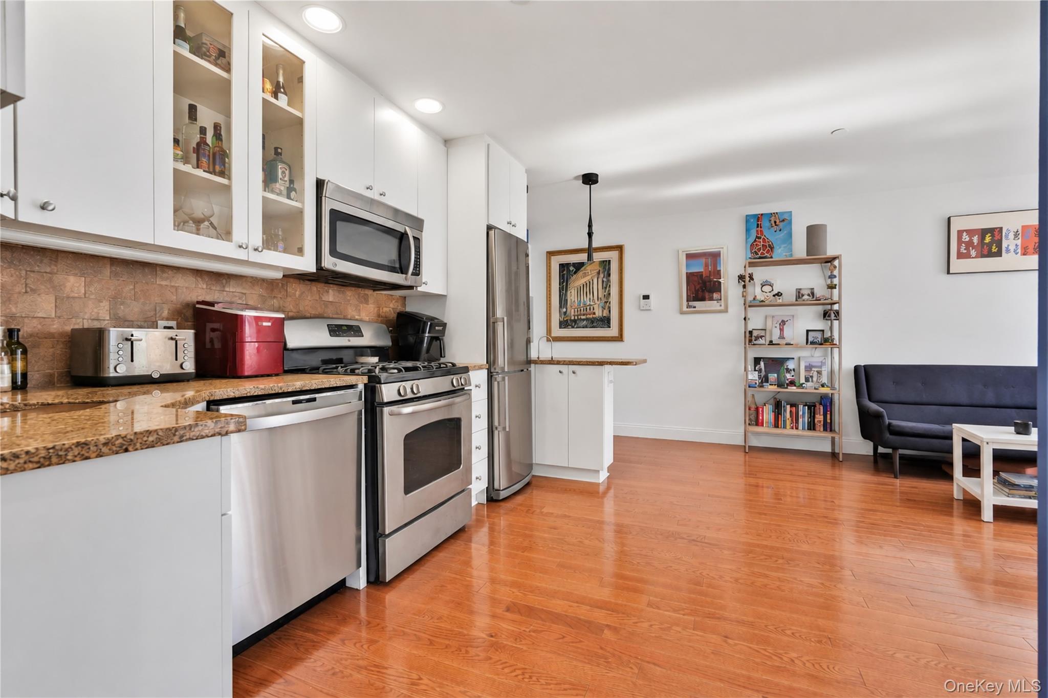 Open-plan kitchen with stainless steel appliances and granite counters beside a living area with hardwood floors.
