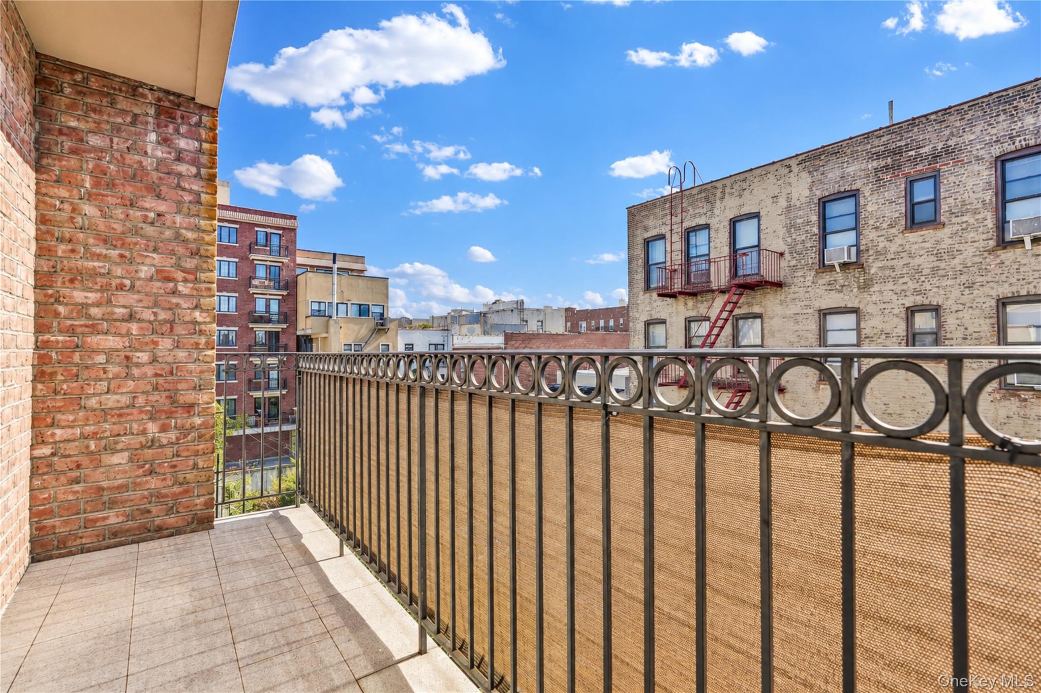 Apartment balcony with tiled flooring and a circular-pattern metal railing overlooking neighboring buildings.