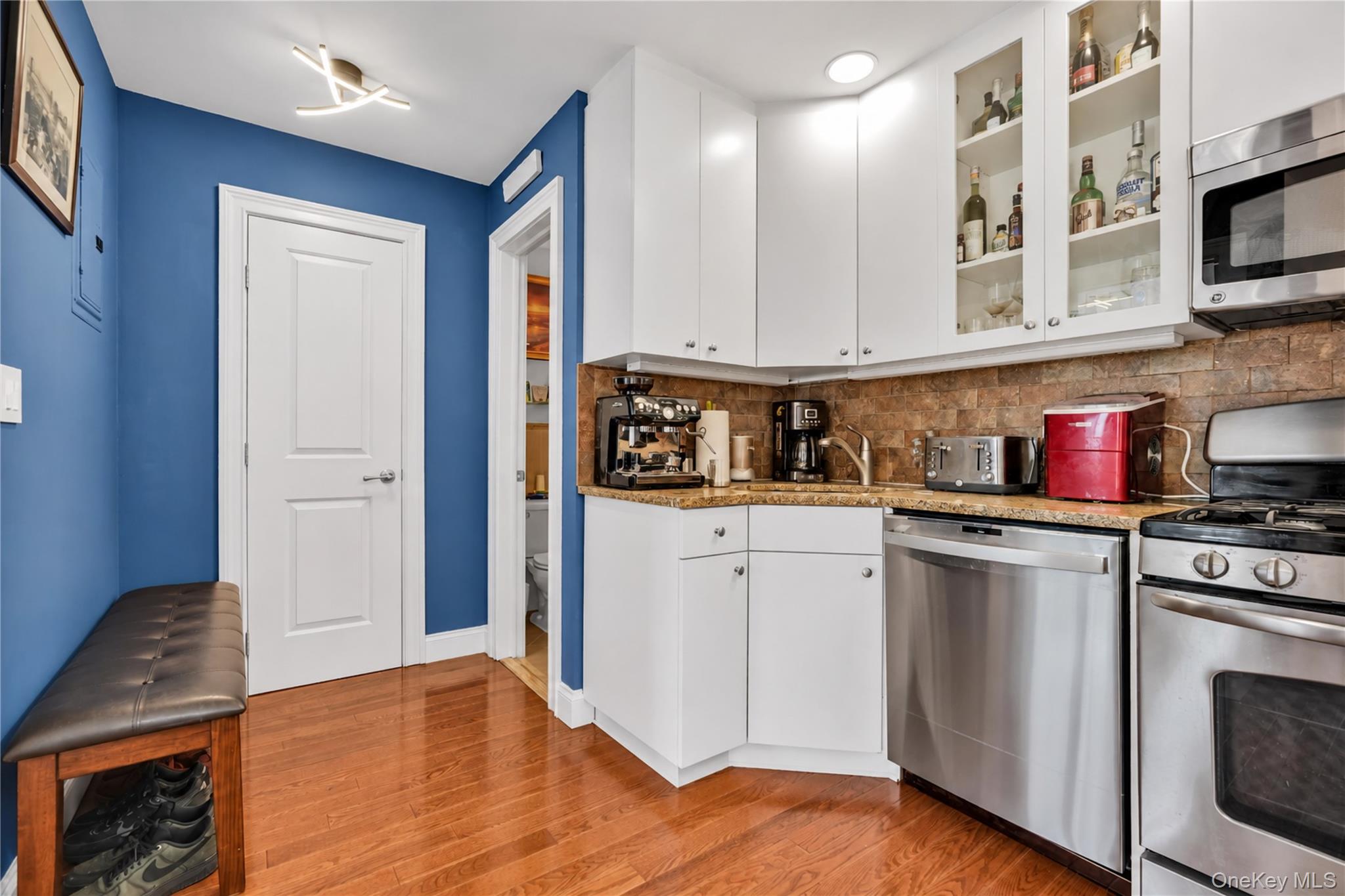 Kitchen with white cabinetry, stainless steel appliances, brown tile backsplash, and blue accent wall.