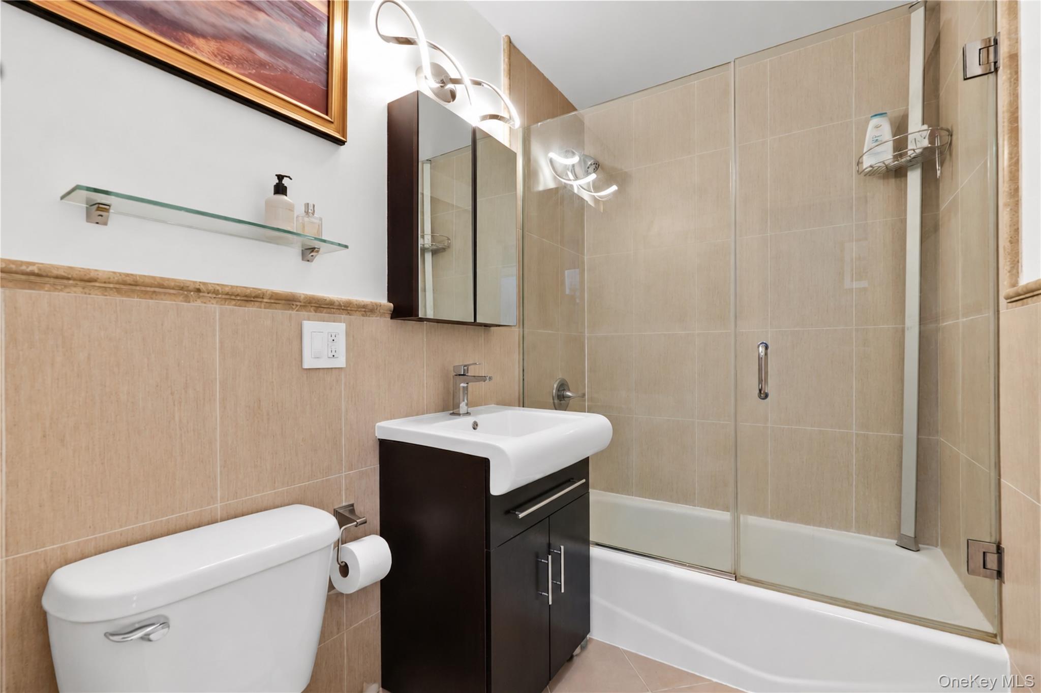 Bathroom with beige tile, glass-enclosed tub and shower, and dark vanity.