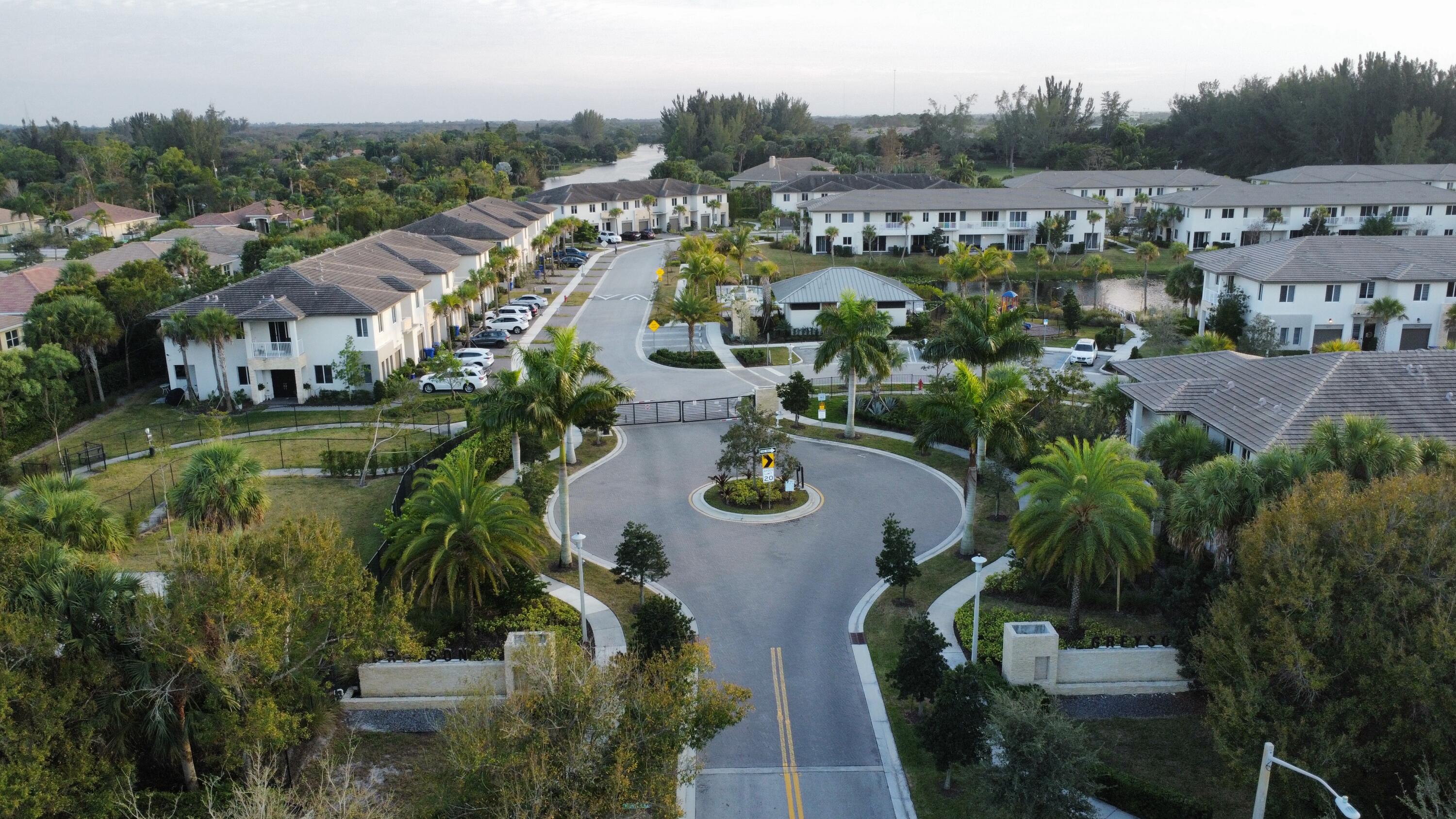 Aerial view of a gated residential community with palm-lined roads and a circular entrance drive.