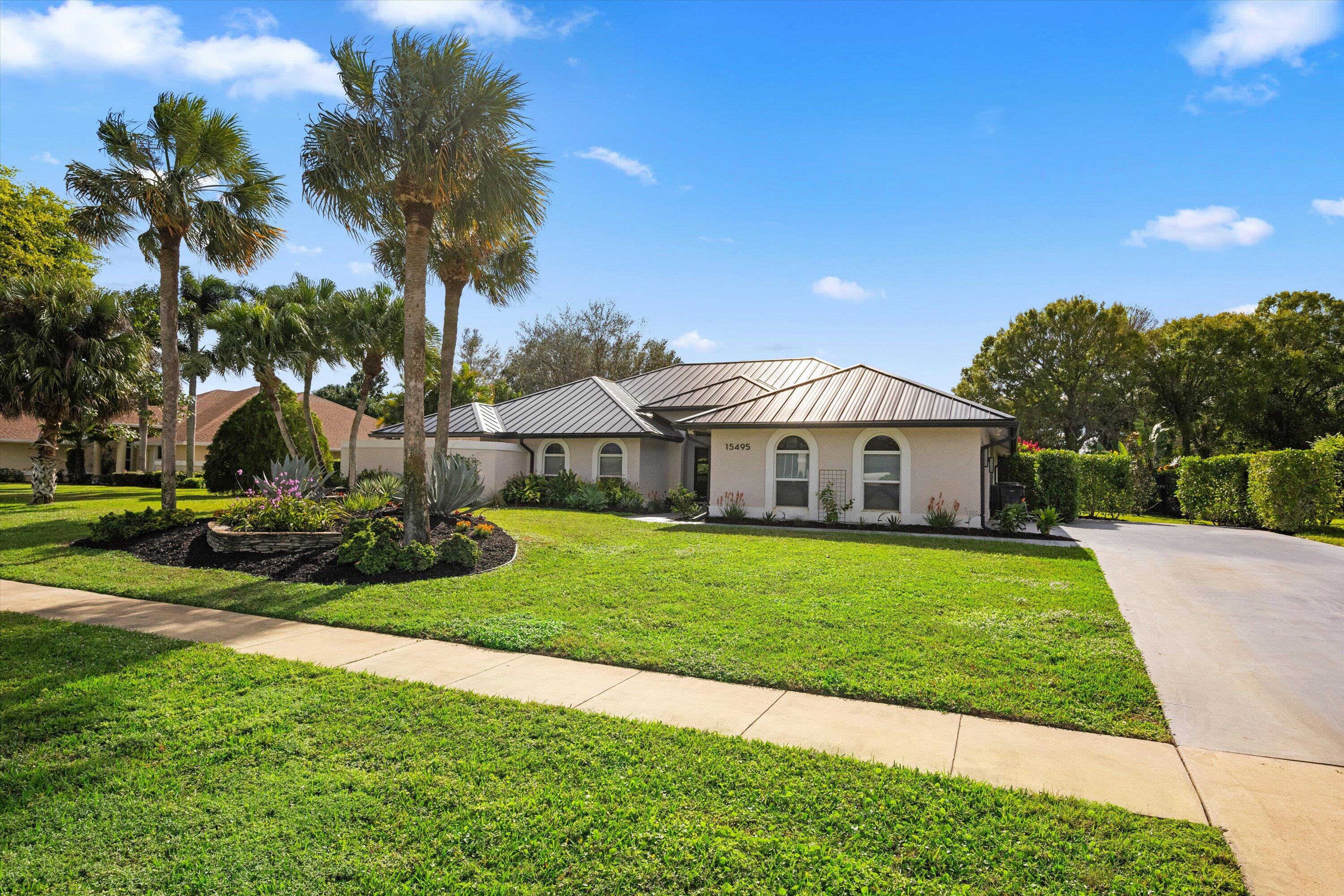 Single-story stucco home with a metal roof, arched windows, and palm trees across the lawn.