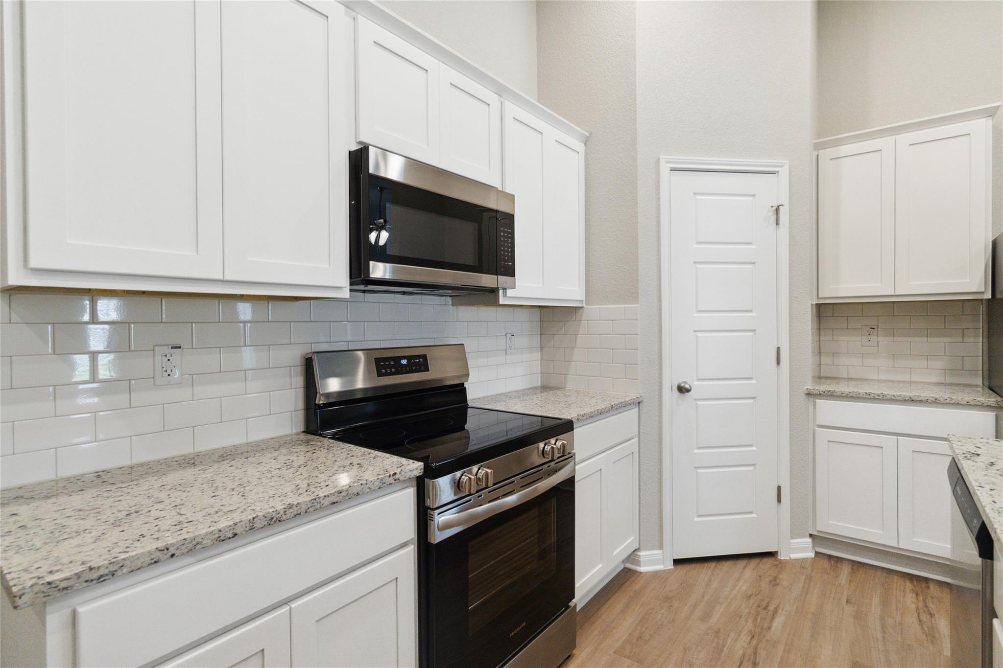Kitchen with white shaker cabinets, subway tile backsplash, stone counters, and a stainless steel range.