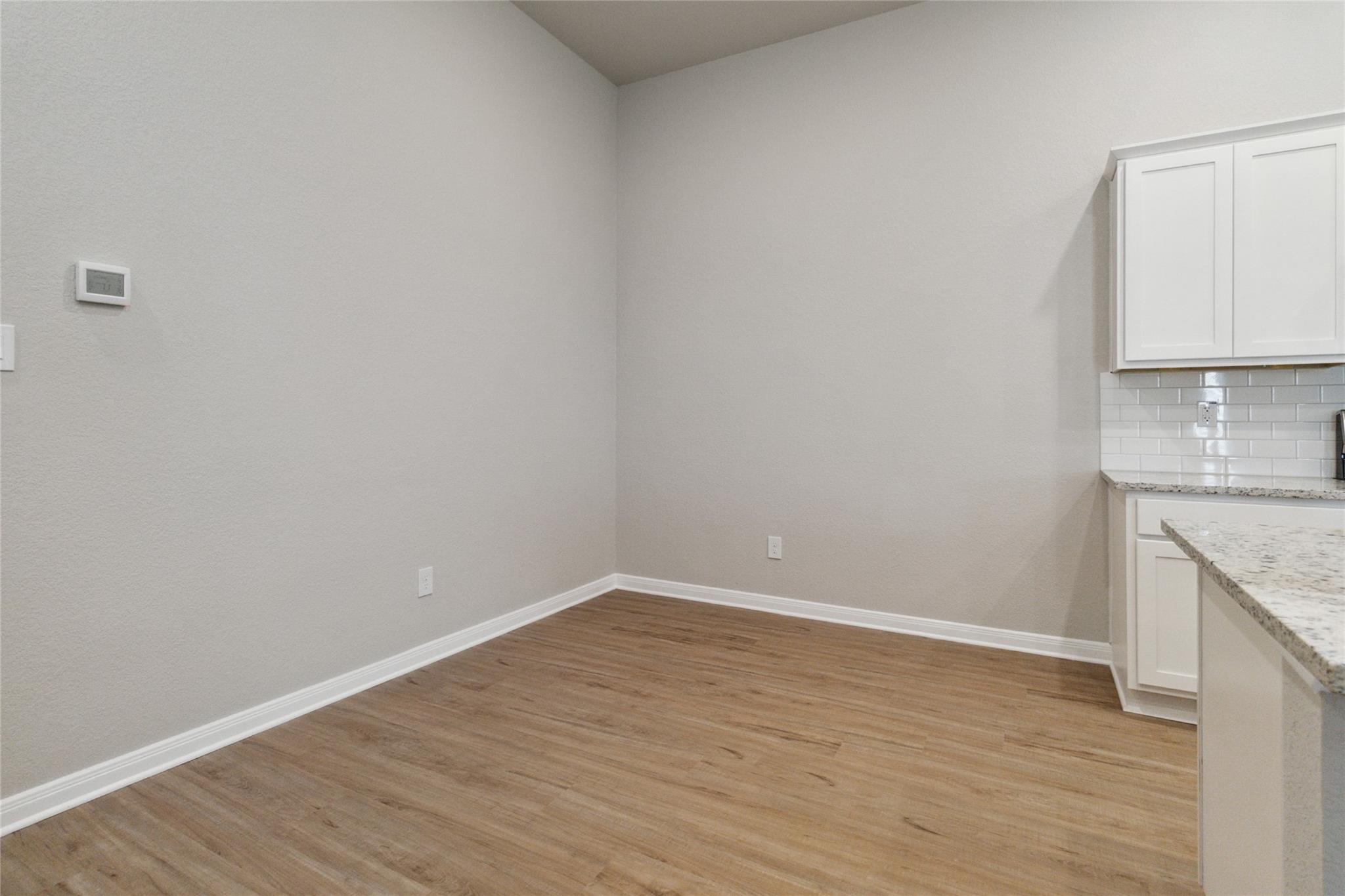 Empty dining area beside a kitchen with wood flooring and white cabinetry.