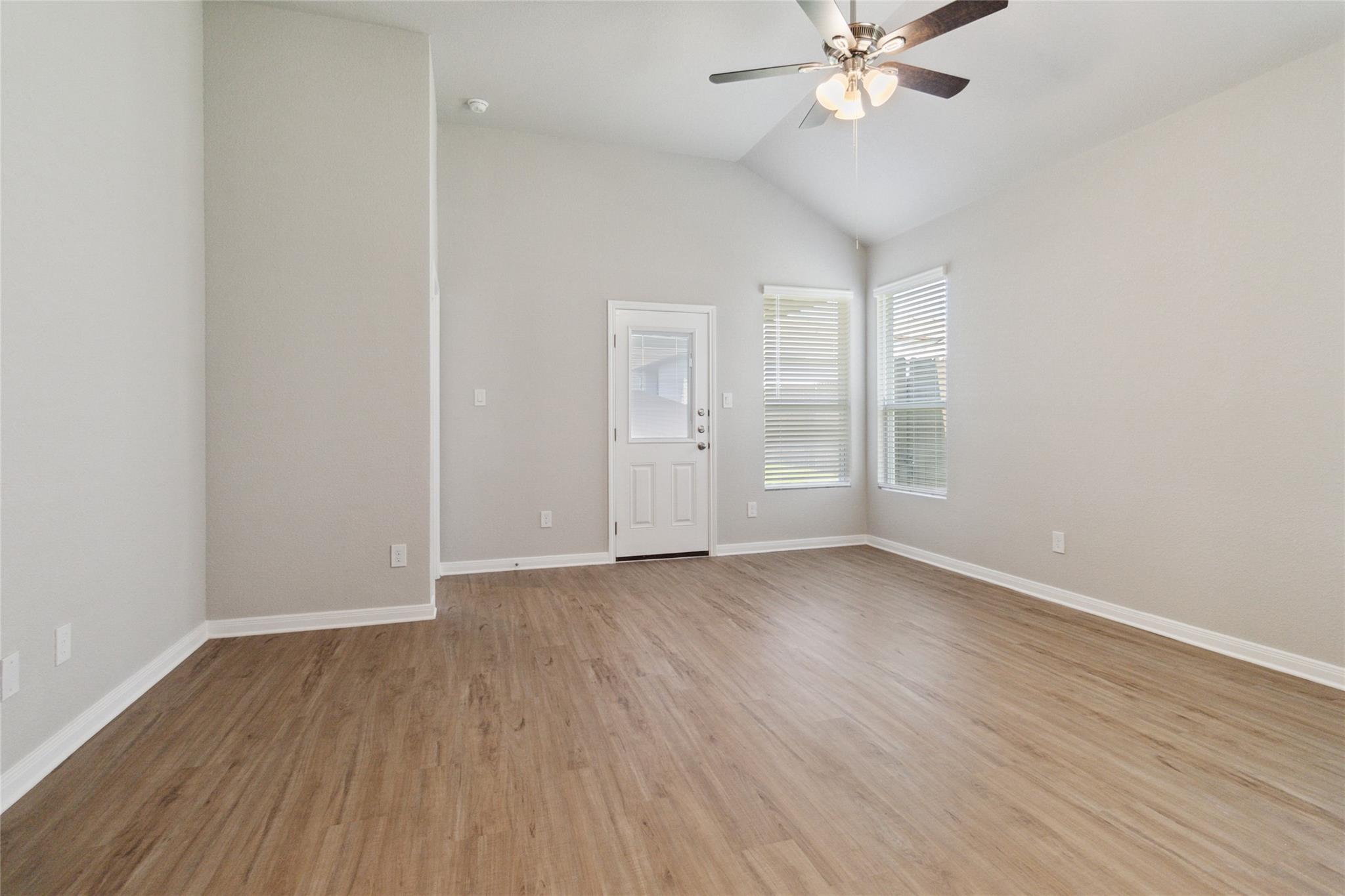 Empty living room with wood-look floors, a white door, two windows, and a ceiling fan.
