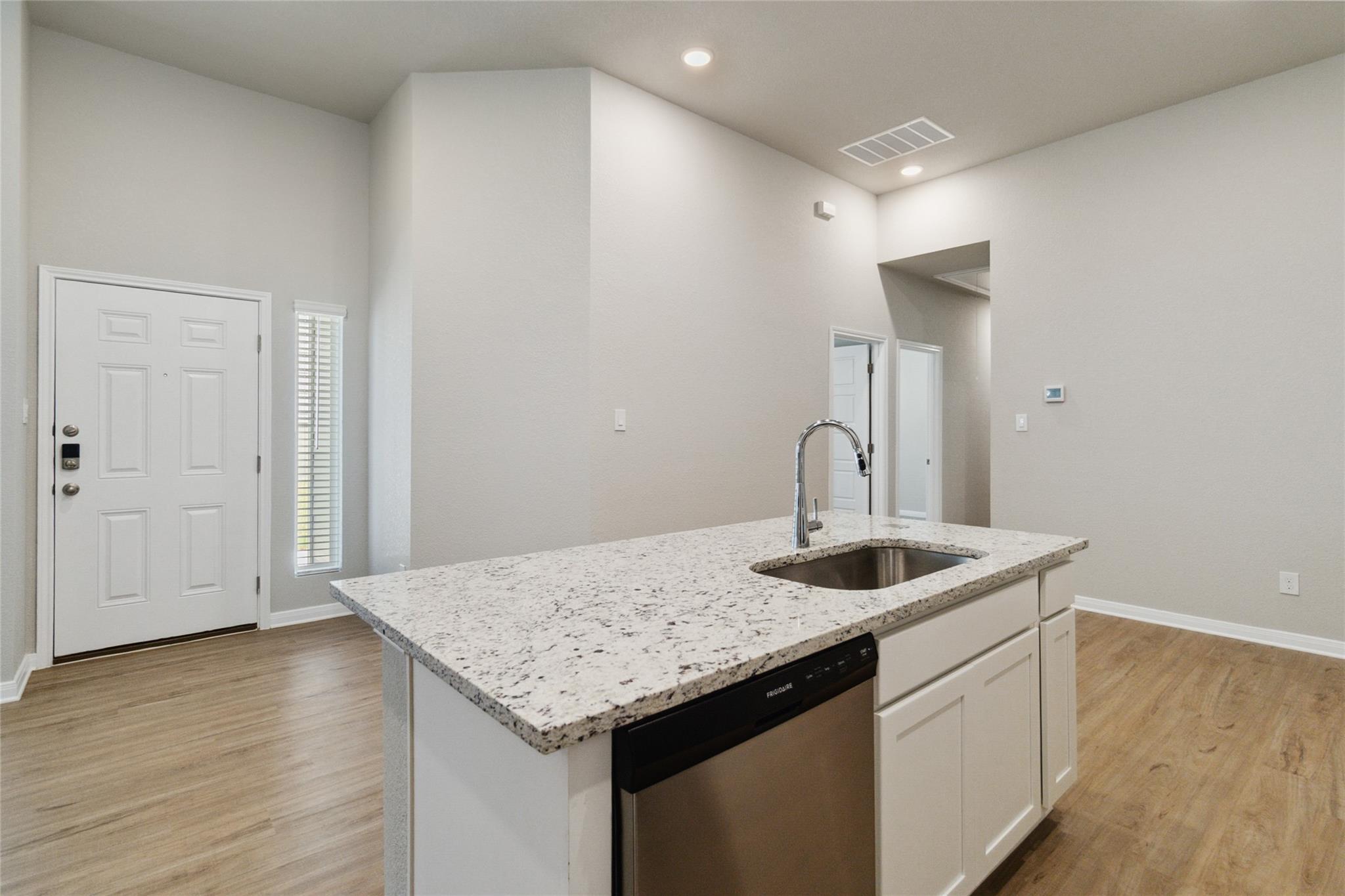 Kitchen with a large speckled granite island, undermount sink, and built-in dishwasher.