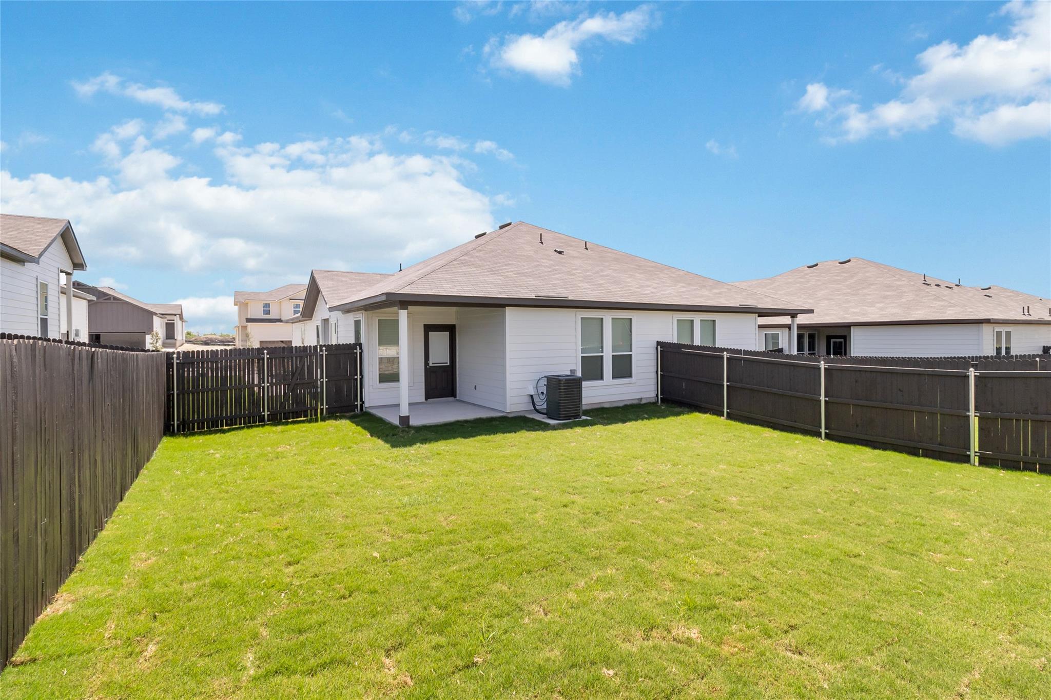 Rear of a single-story home with a covered patio and fenced grassy backyard.