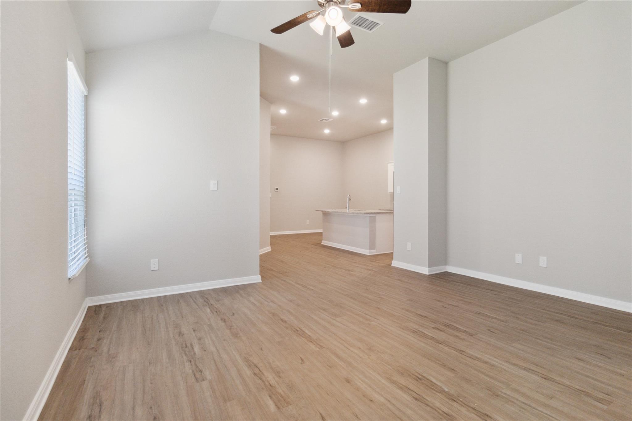 Empty open-plan living area with wood-look floors, ceiling fan, and kitchen island.
