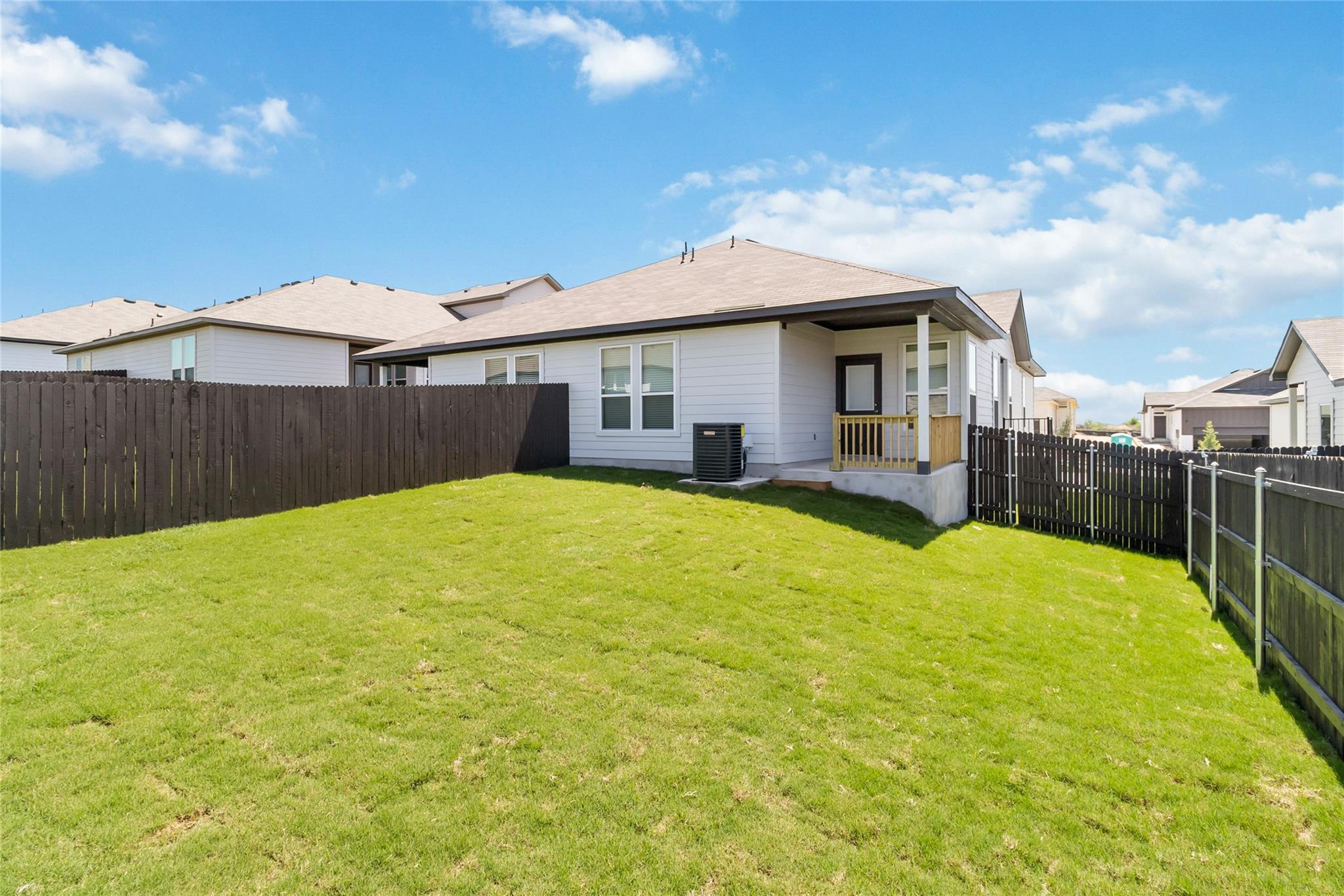 Backyard with a broad green lawn, dark fencing, and a covered porch on a single-story house.