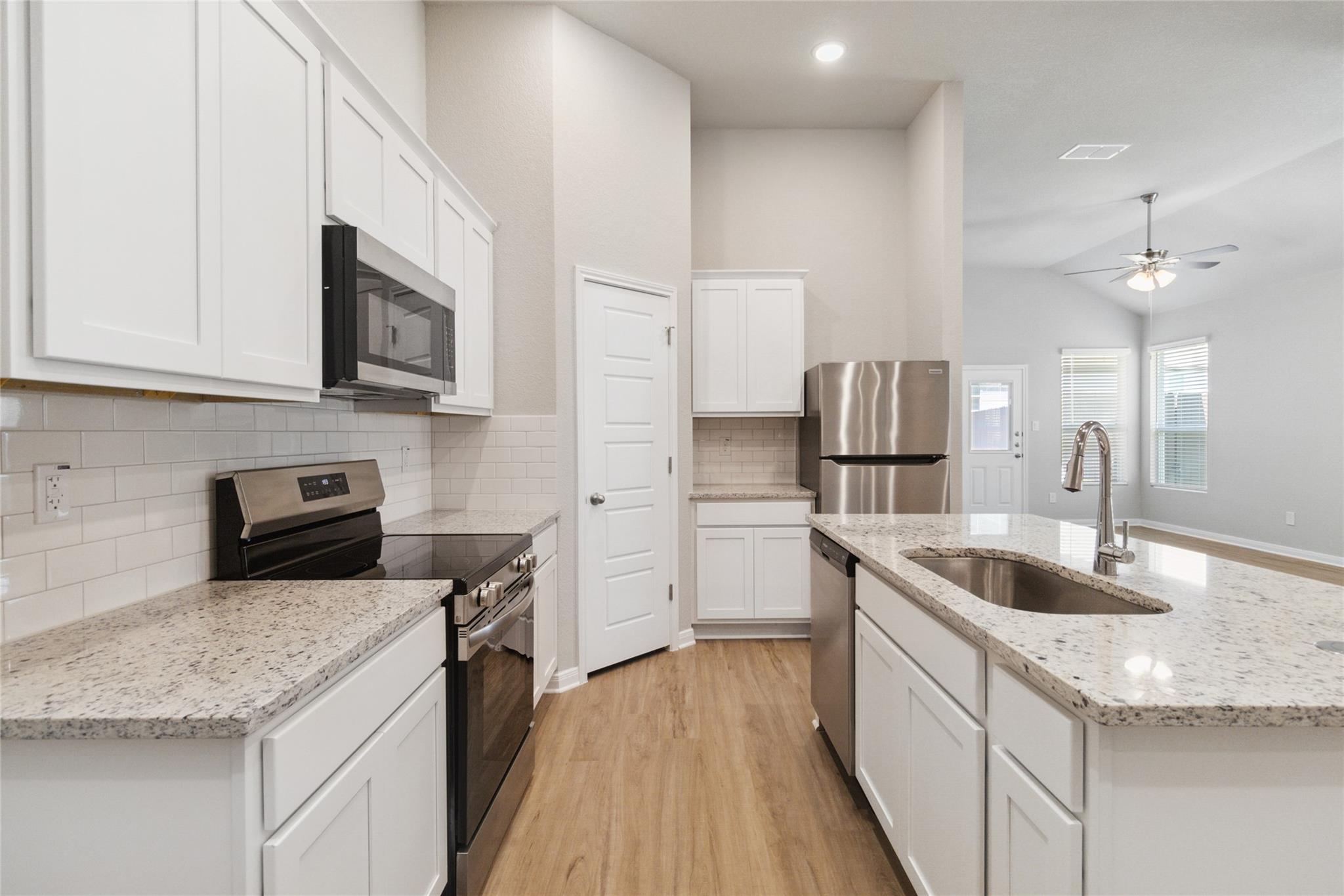 Kitchen with white cabinets, granite island, stainless appliances, and wood-look floors.