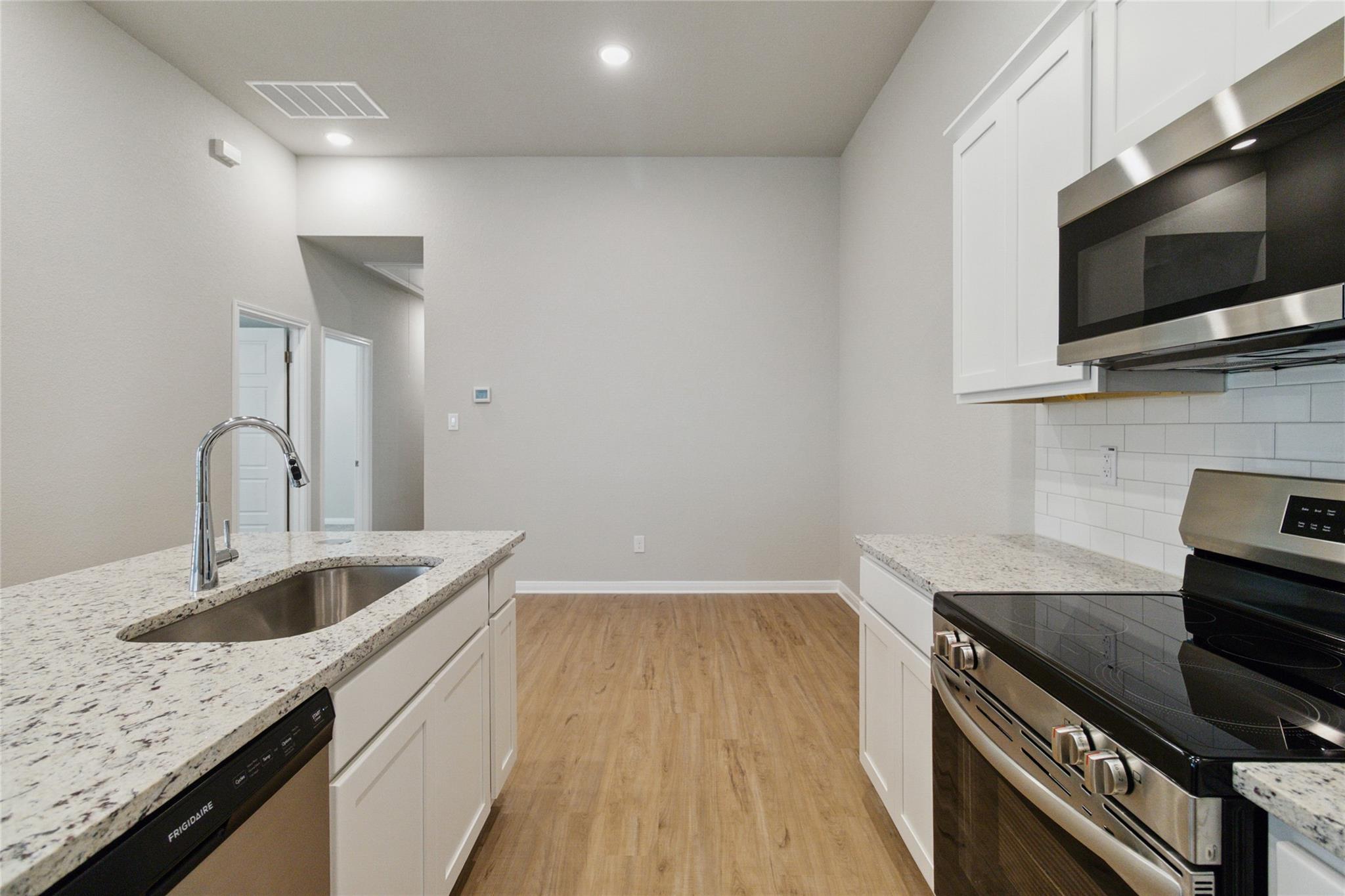 Kitchen with white cabinets, granite counters, stainless appliances, and wood-look flooring.