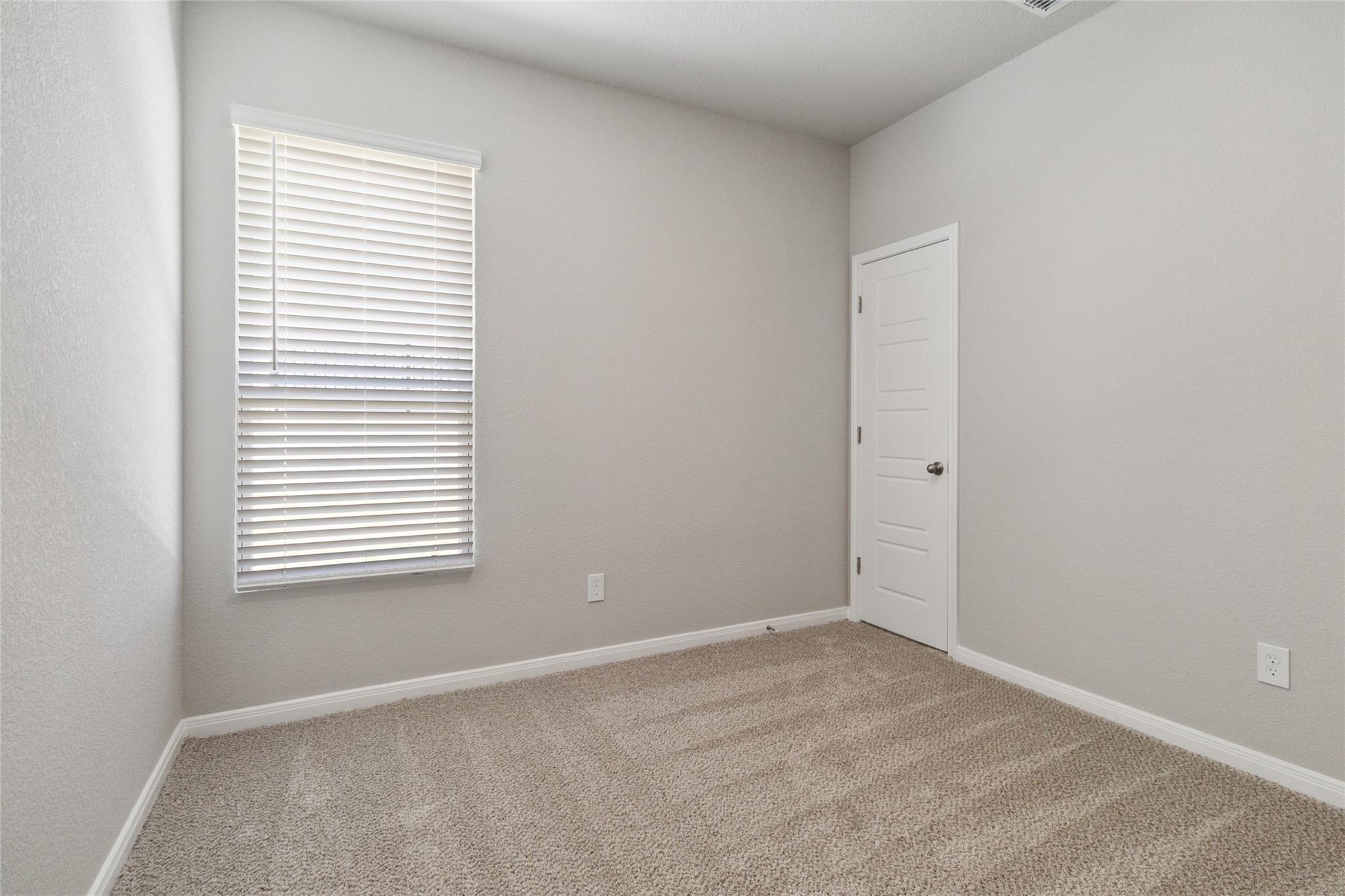 Empty carpeted room with a window and white blinds beside a closed door.