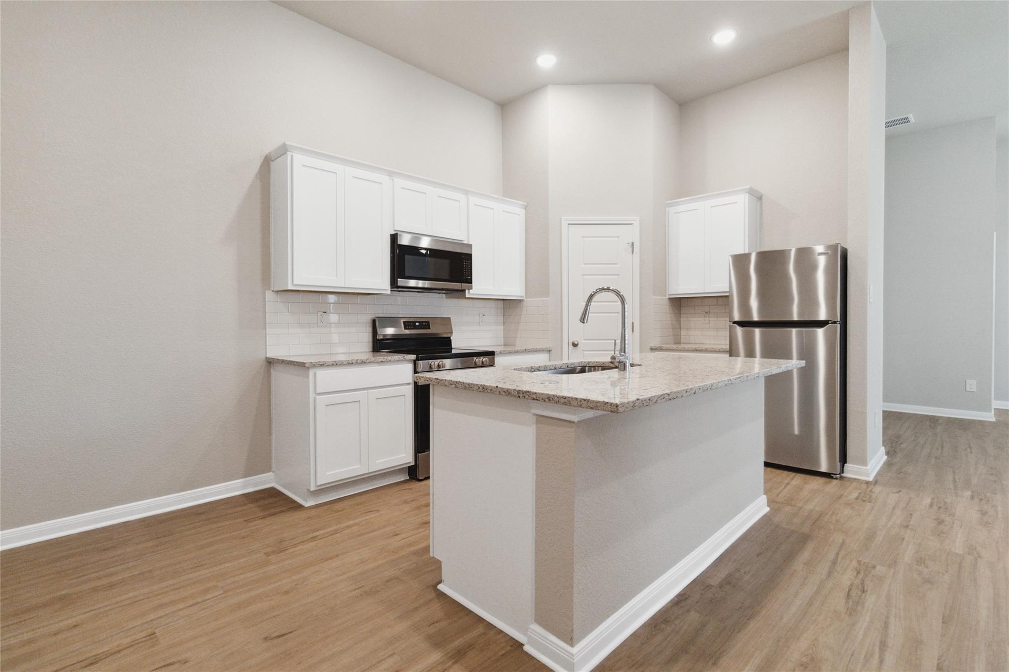 Kitchen with white cabinets, granite island and sink, stainless steel appliances, and wood-look flooring.