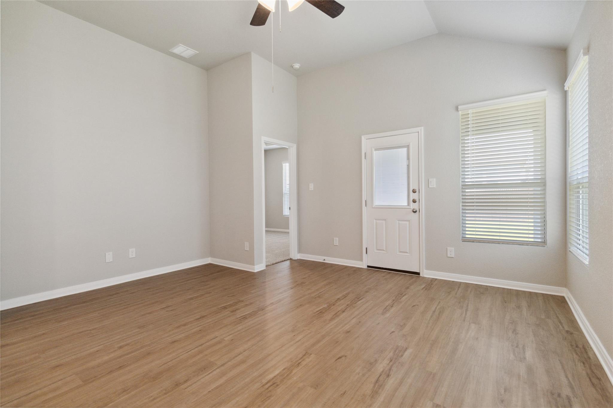Empty living area with wood-look flooring, a high ceiling, and a white exterior door beside two windows.