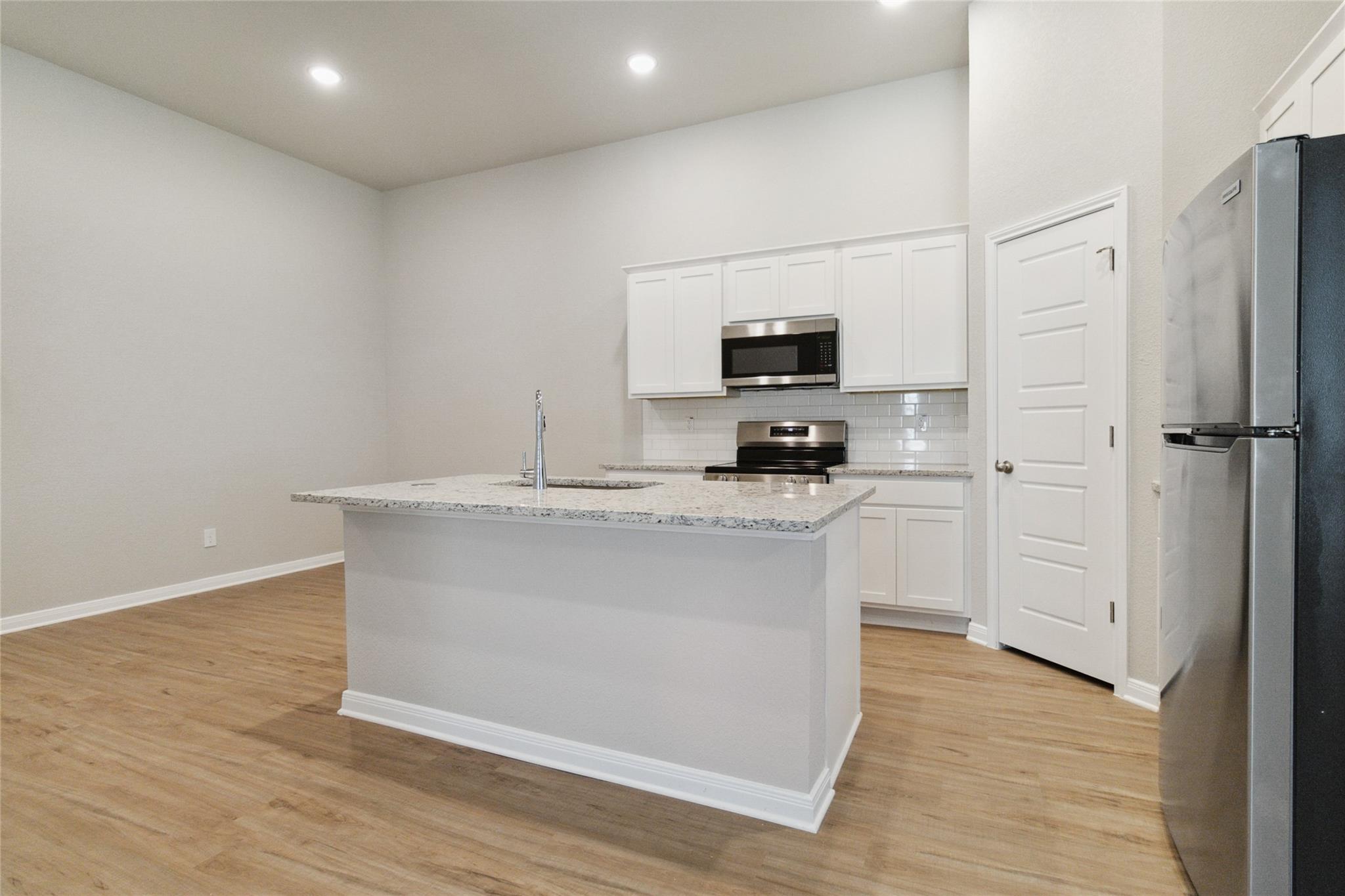 Kitchen with a large granite island, white cabinets, stainless steel appliances, and wood-look flooring.