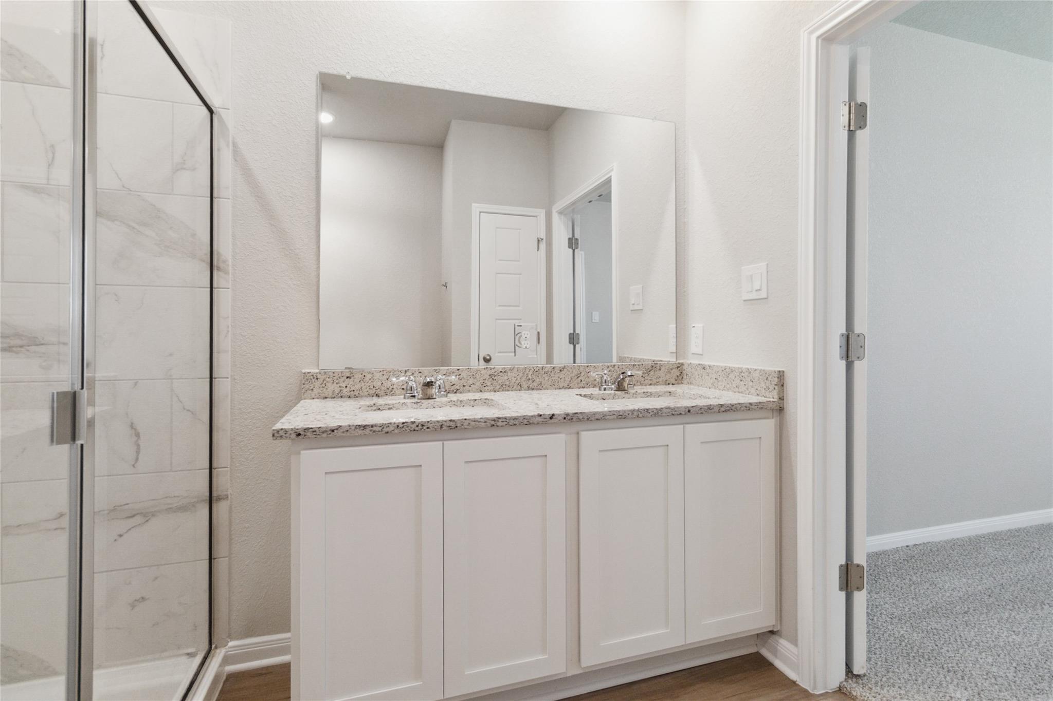 Bathroom with a double-sink vanity, speckled countertop, and glass shower with marble-look tile.