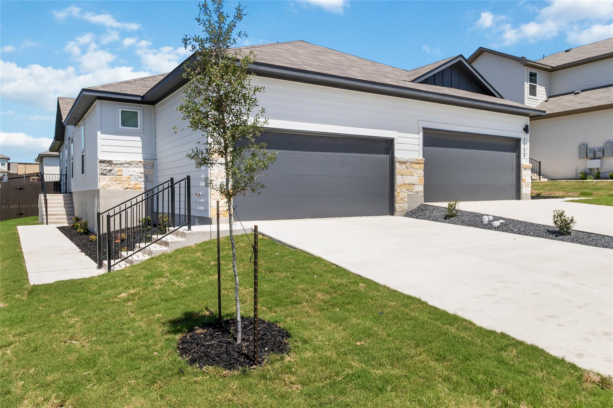 White single-story home with two dark garage doors, stone accents, and a broad driveway.