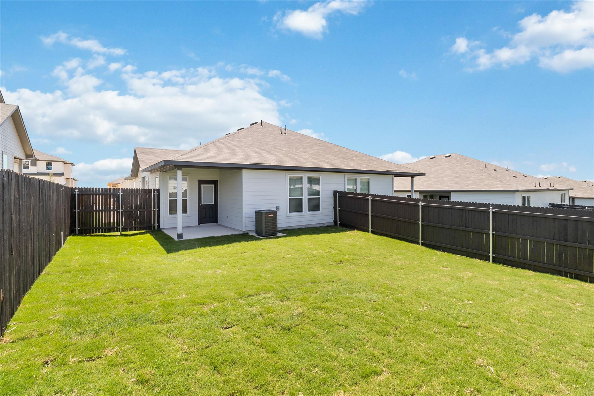 Single-story home behind a fenced grassy backyard, with a covered back entry and neighboring houses beyond.