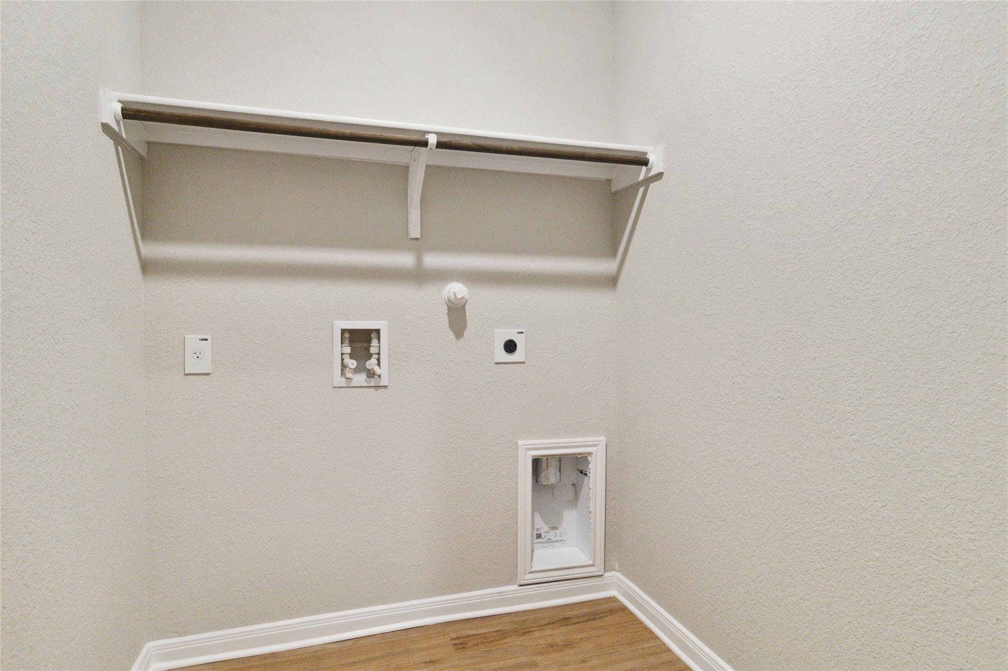 Empty laundry closet with washer and dryer hookups, a high shelf, and wood-look flooring.