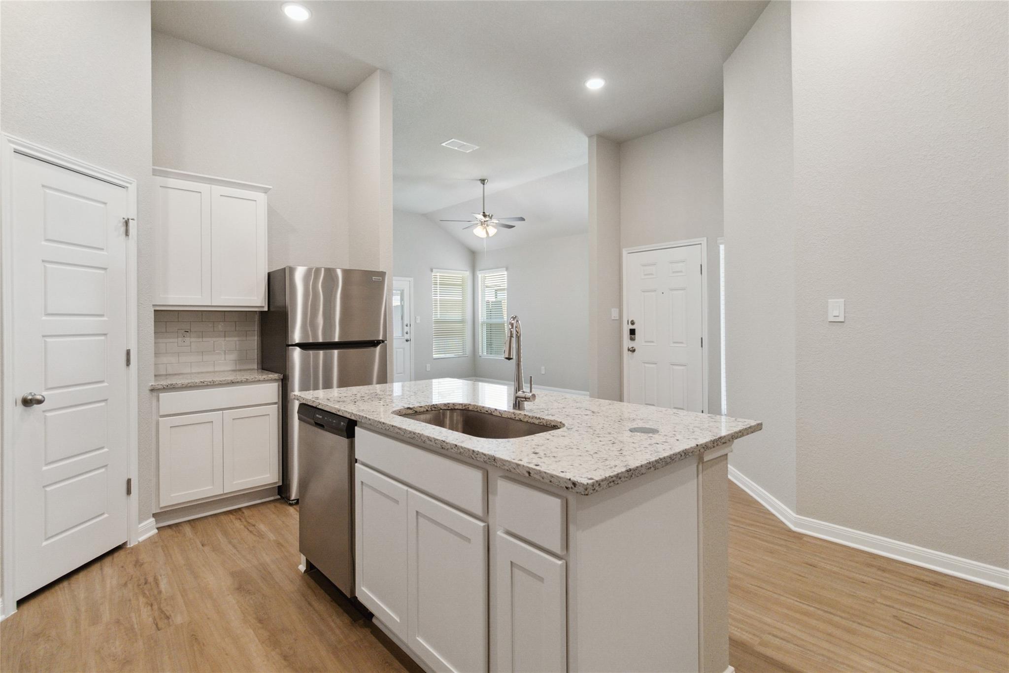 Kitchen with a granite island sink, white cabinets, stainless steel appliances, and wood-look floors.