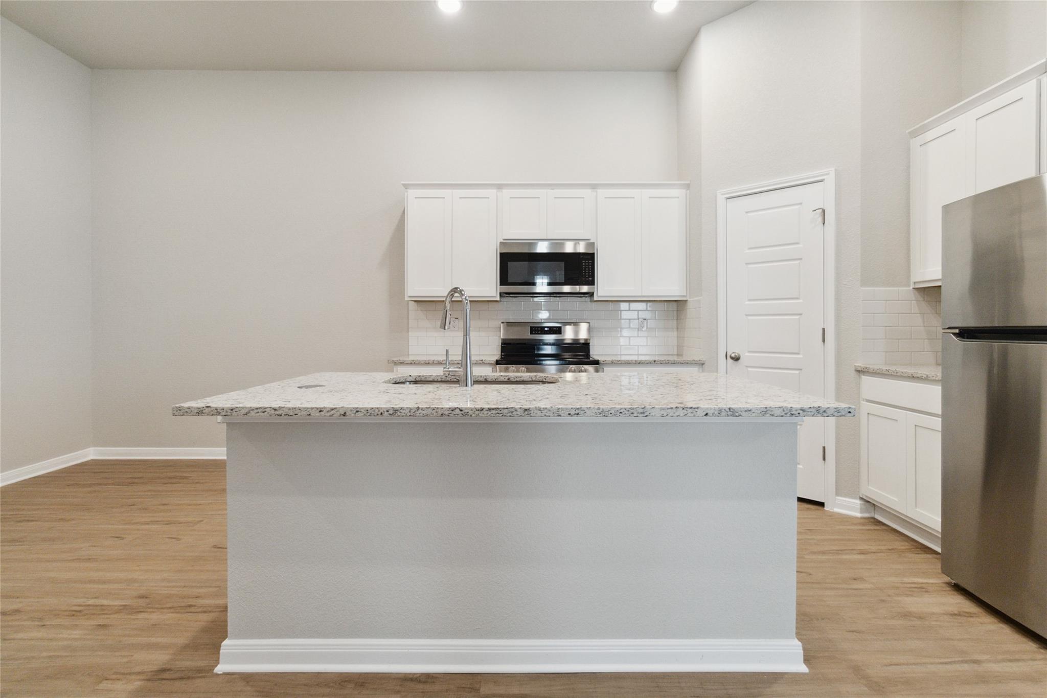 Kitchen with a large stone island, white cabinets, stainless steel appliances, and wood-look floors.