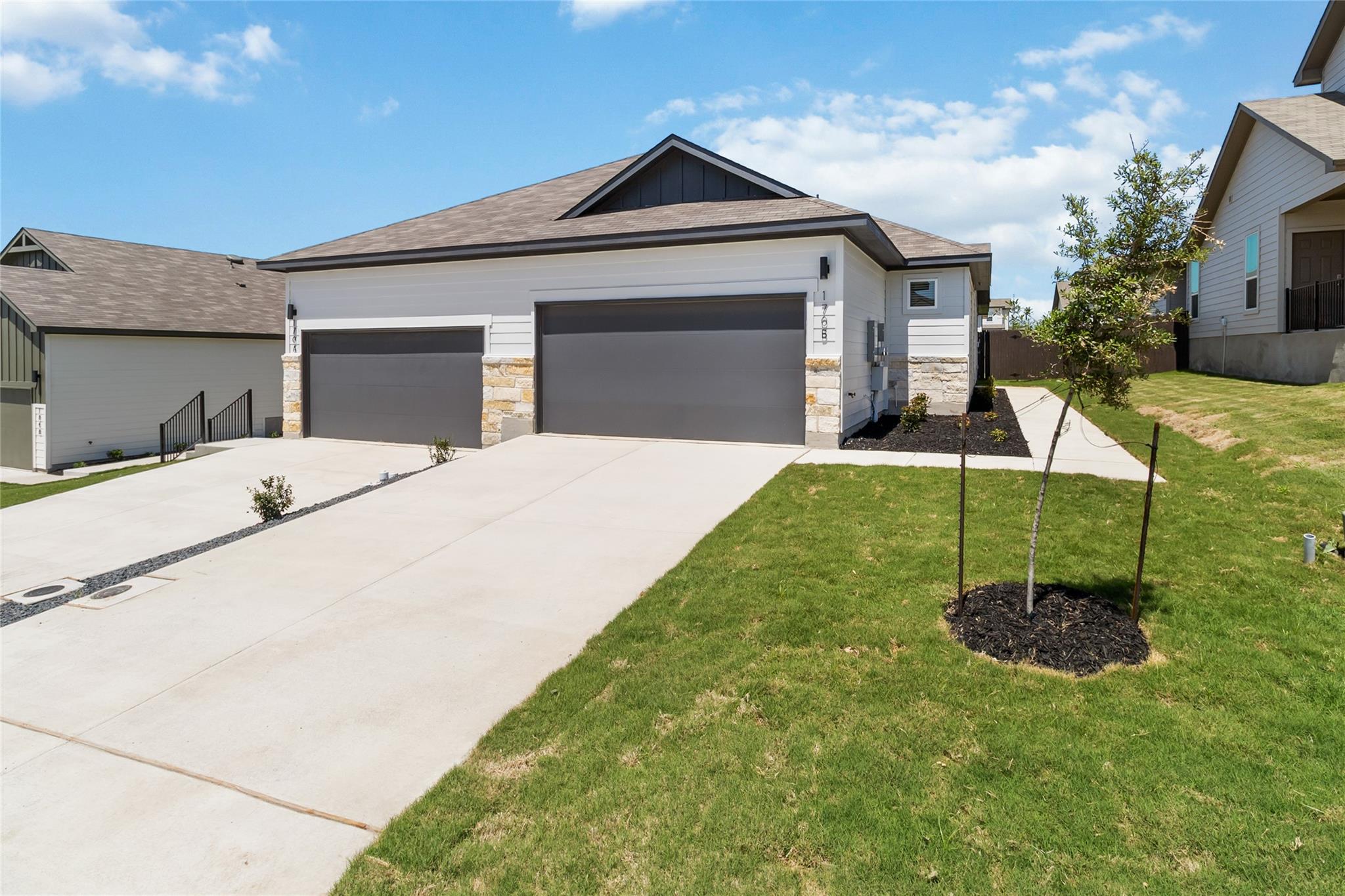 White house with stone accents and two gray garage doors, fronted by a wide driveway and lawn.