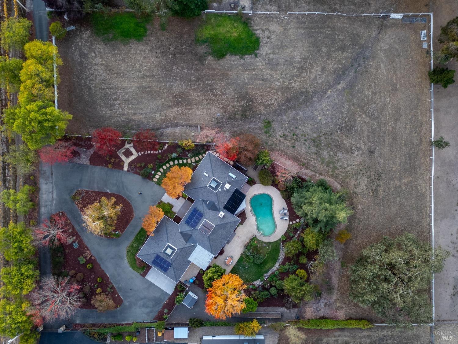 Aerial view of a home, swimming pool, landscaped grounds, and expansive fenced field.