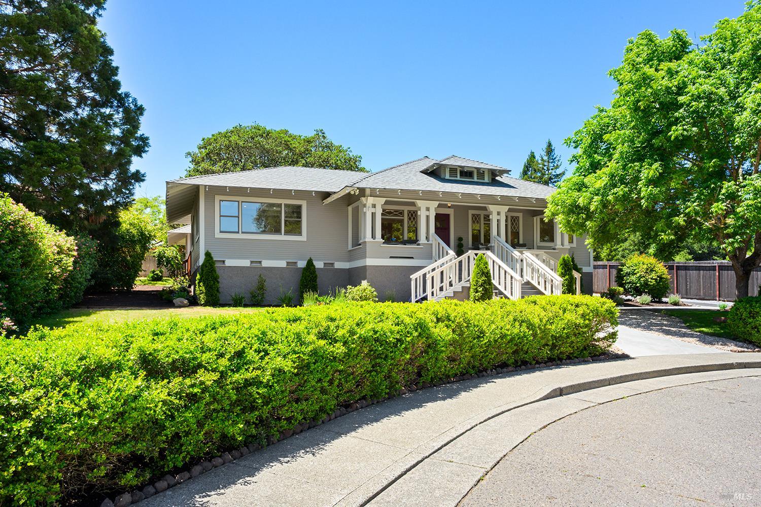 Gray Craftsman-style house with a covered porch, white railings, and landscaped front yard.