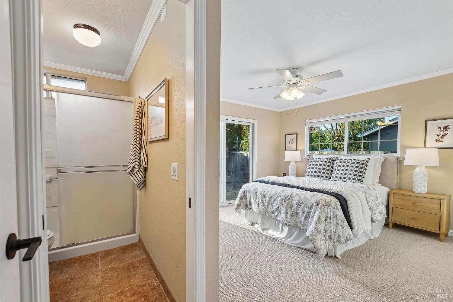 Bedroom with a patterned bedspread, wide window, sliding glass door, and adjoining bathroom.