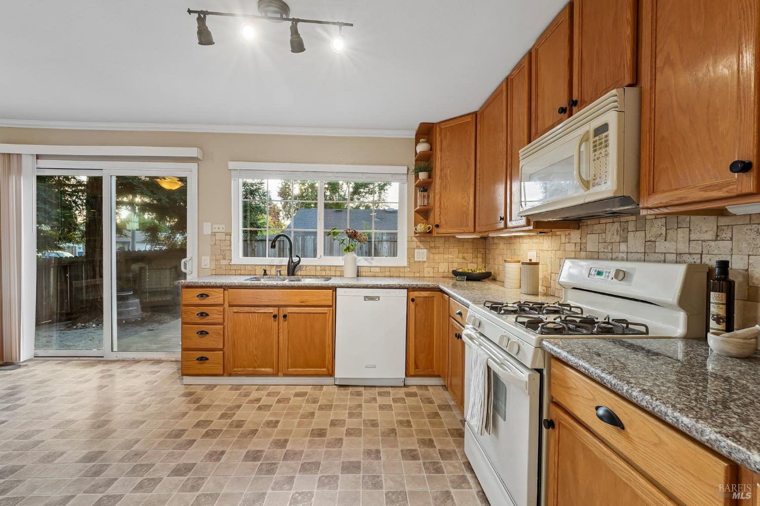 Kitchen with honey-toned cabinets, tiled backsplash, white appliances, and a sliding glass door.