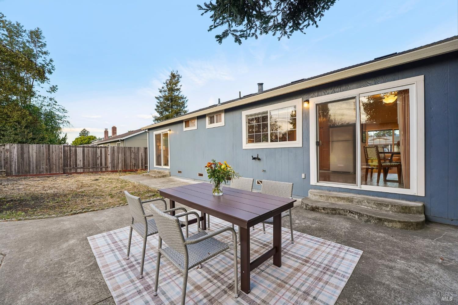 Blue-sided home with a patio dining set and sliding glass doors opening onto a fenced yard.