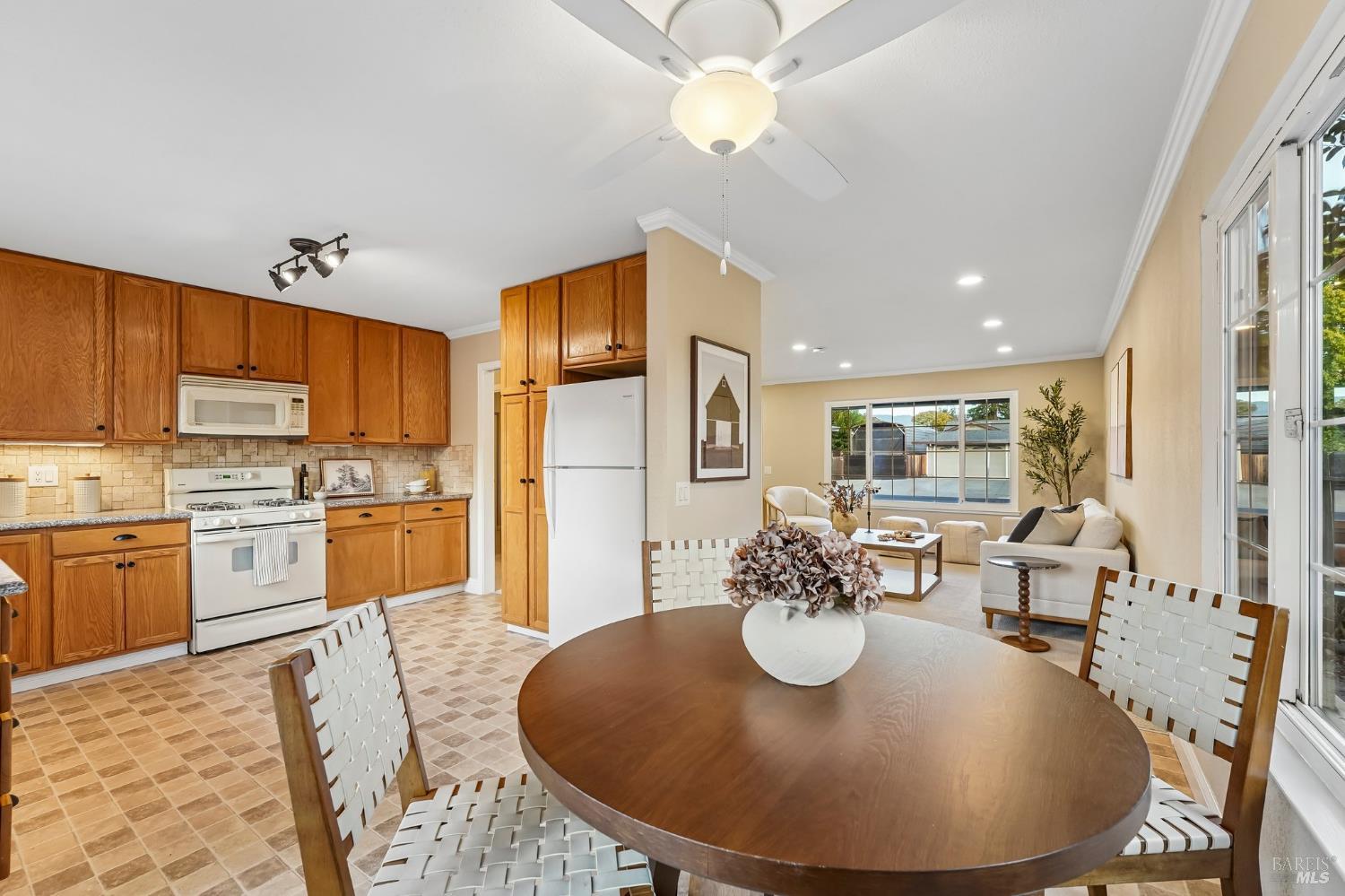 Open-plan kitchen and living room with warm wood cabinets, a round dining table, and views of a backyard pool.