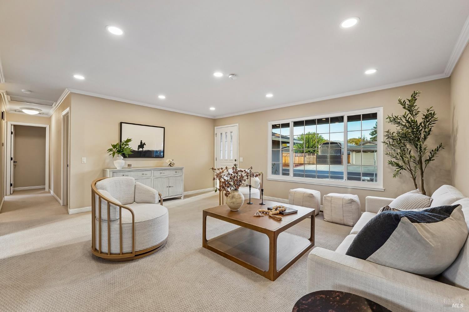 Staged living room with a white sofa, wood coffee table, and large window overlooking a backyard.