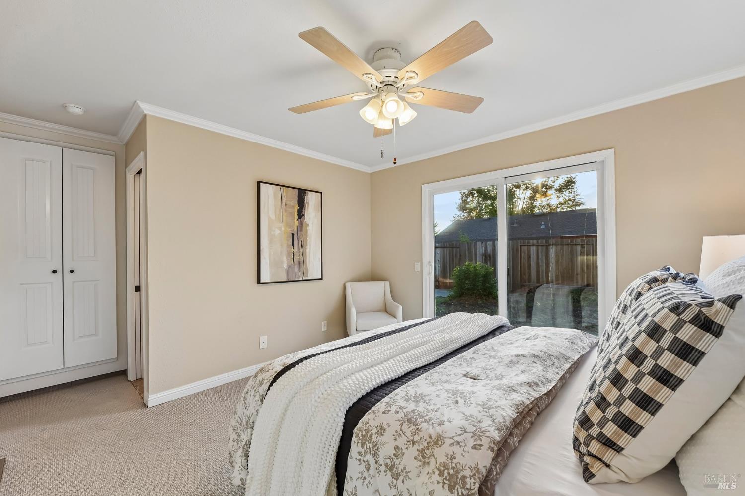 Furnished bedroom with patterned bedding, a ceiling fan, and sliding glass doors to a fenced yard.