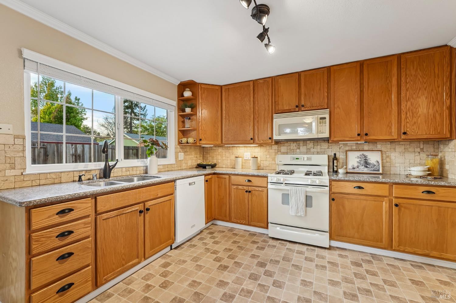 Kitchen with honey-colored wood cabinets, a wide window above the sink, and white appliances.