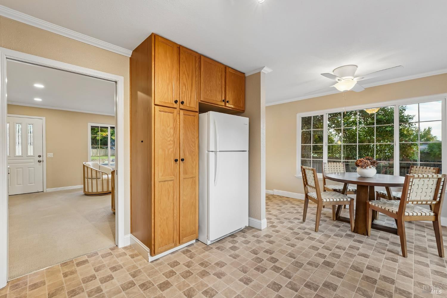 Kitchen and dining area with wood cabinets, tiled floors, and a round table beside large windows.