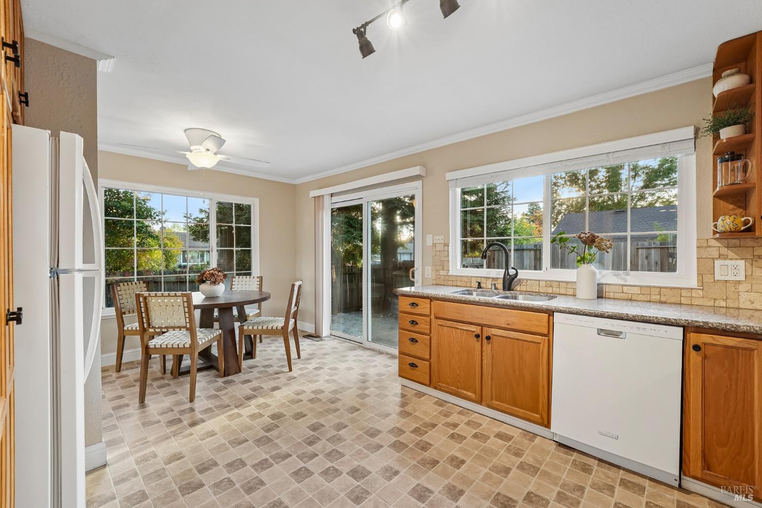 Kitchen and dining area with wood cabinets, tiled floors, and a large window above the sink.