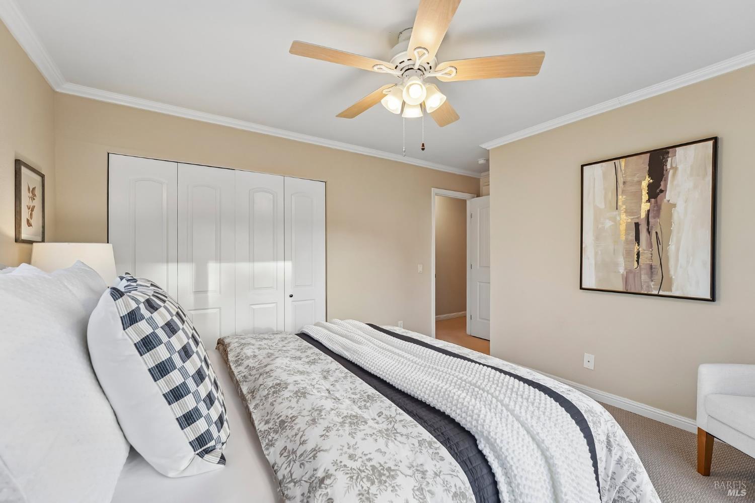 Bedroom with patterned bedding, white closet doors, and a lighted ceiling fan.