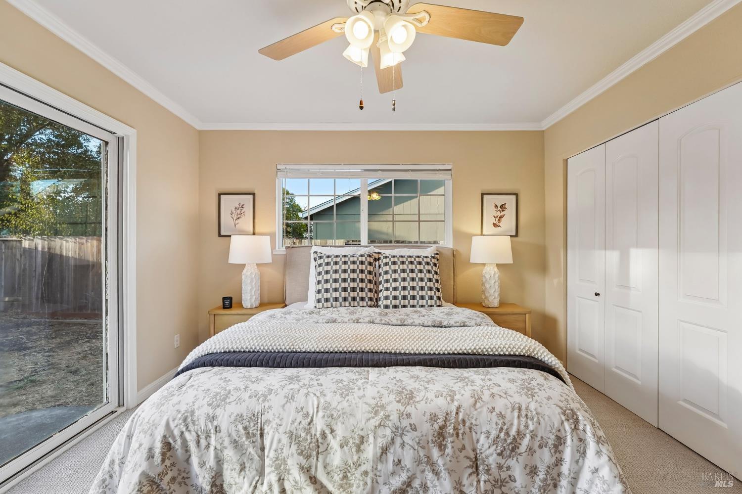 Bedroom with floral bedding, matching bedside lamps, white closet, and sliding glass door.