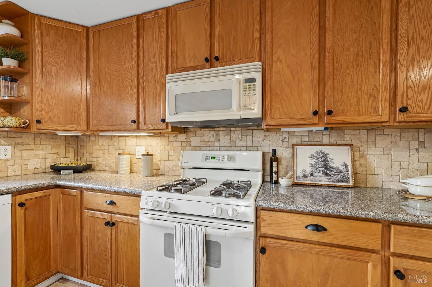 Kitchen with oak cabinetry, granite counters, stone tile backsplash, and a white gas range.
