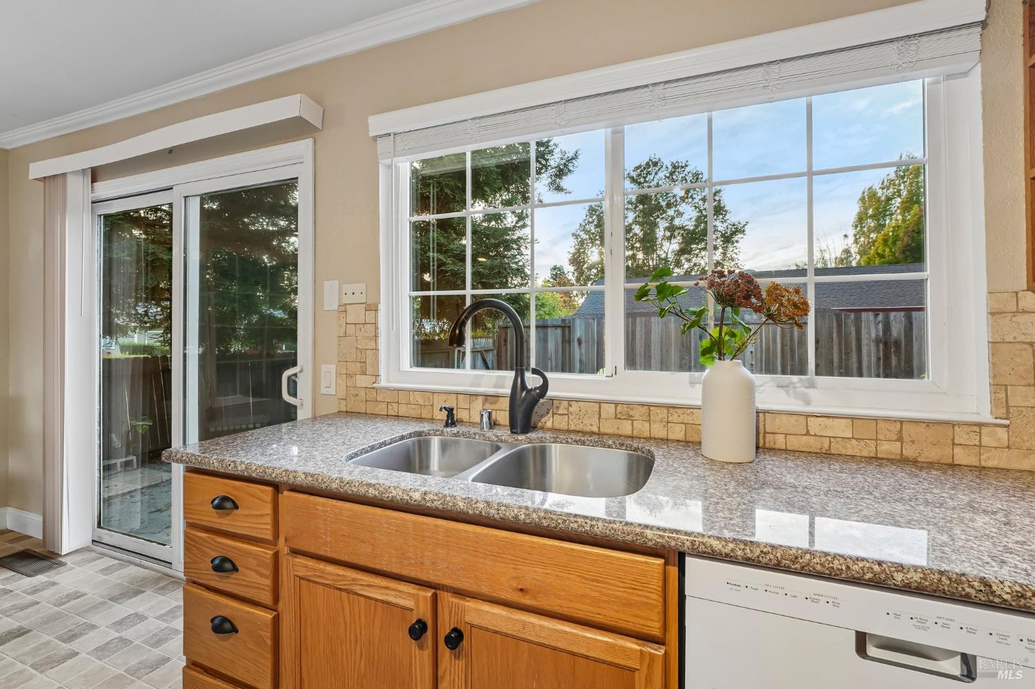 Kitchen with wood cabinets, a double sink, granite counters, and a large backyard-facing window.