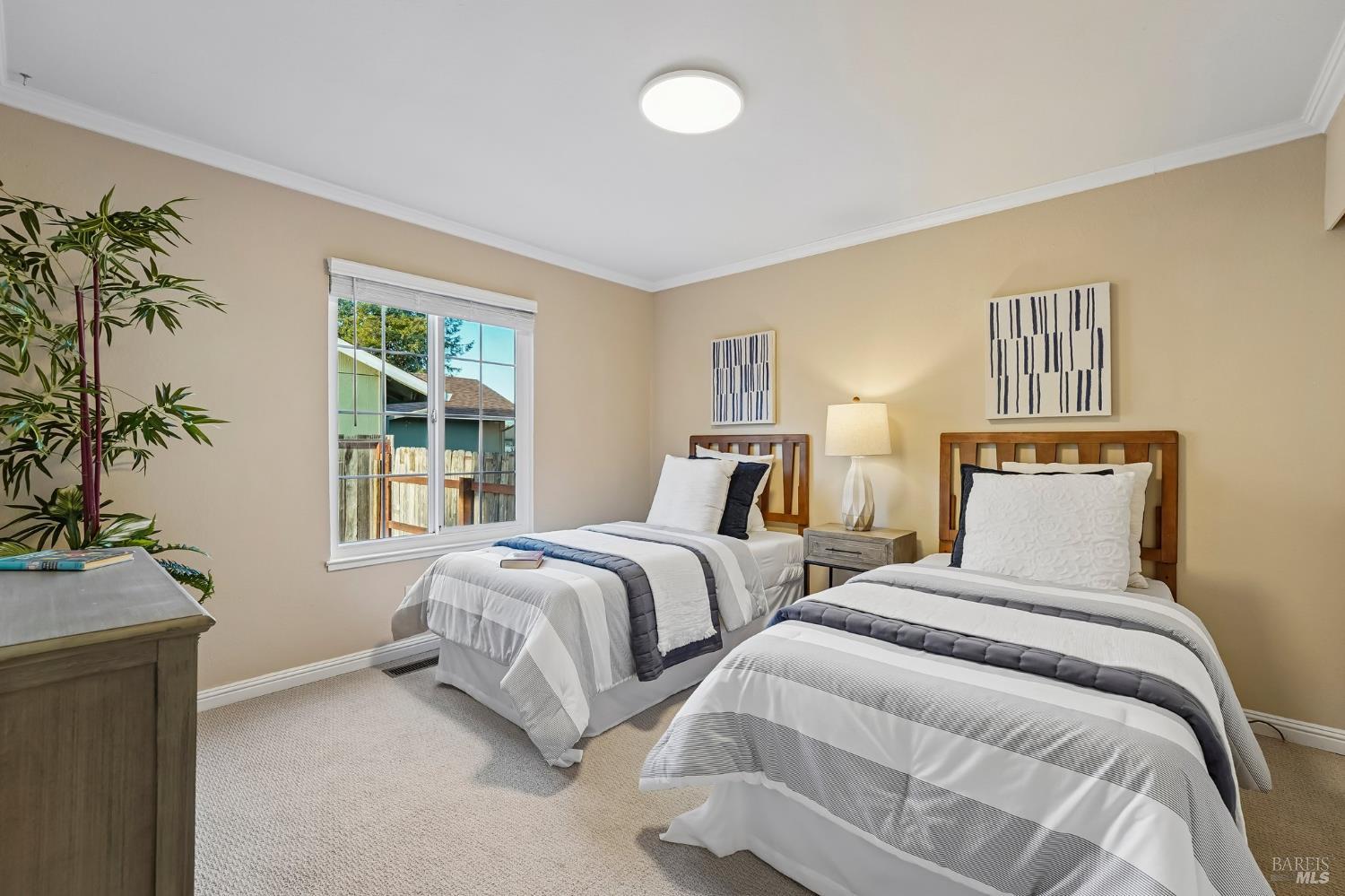 Bedroom with two separate beds, matching wooden headboards, and a window overlooking a fenced yard.