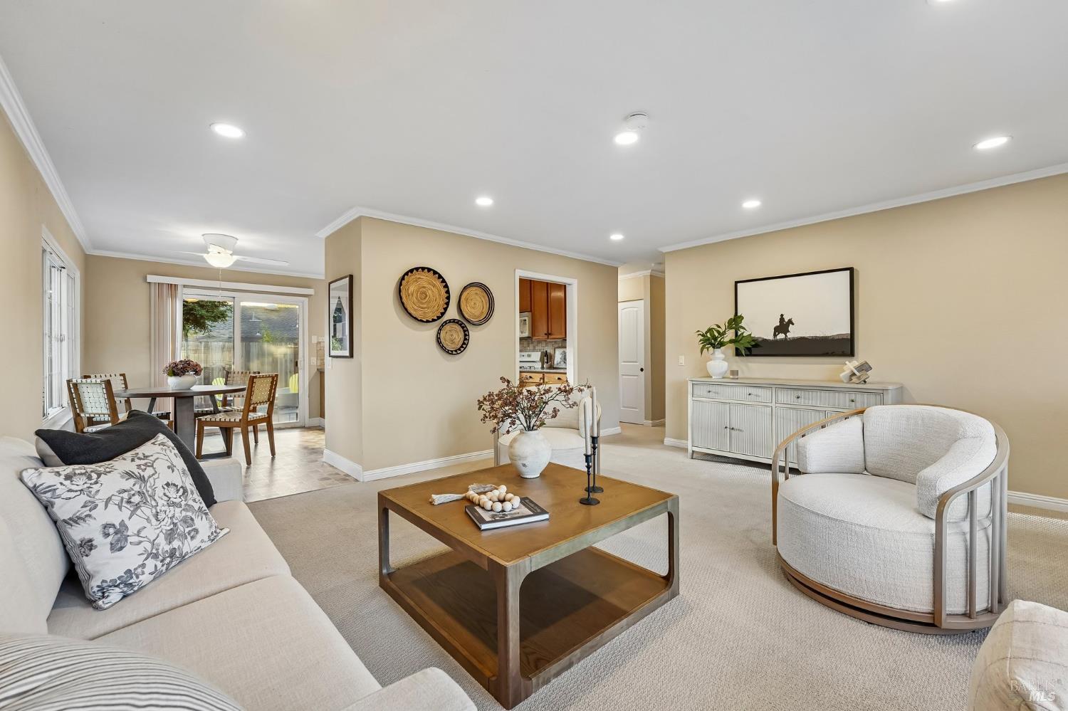 Staged living room with a wood coffee table, curved armchair, and dining area by sliding glass doors.