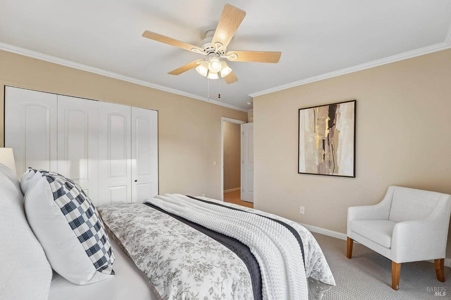 Bedroom with patterned bedding, white closet doors, ceiling fan, and an armchair.