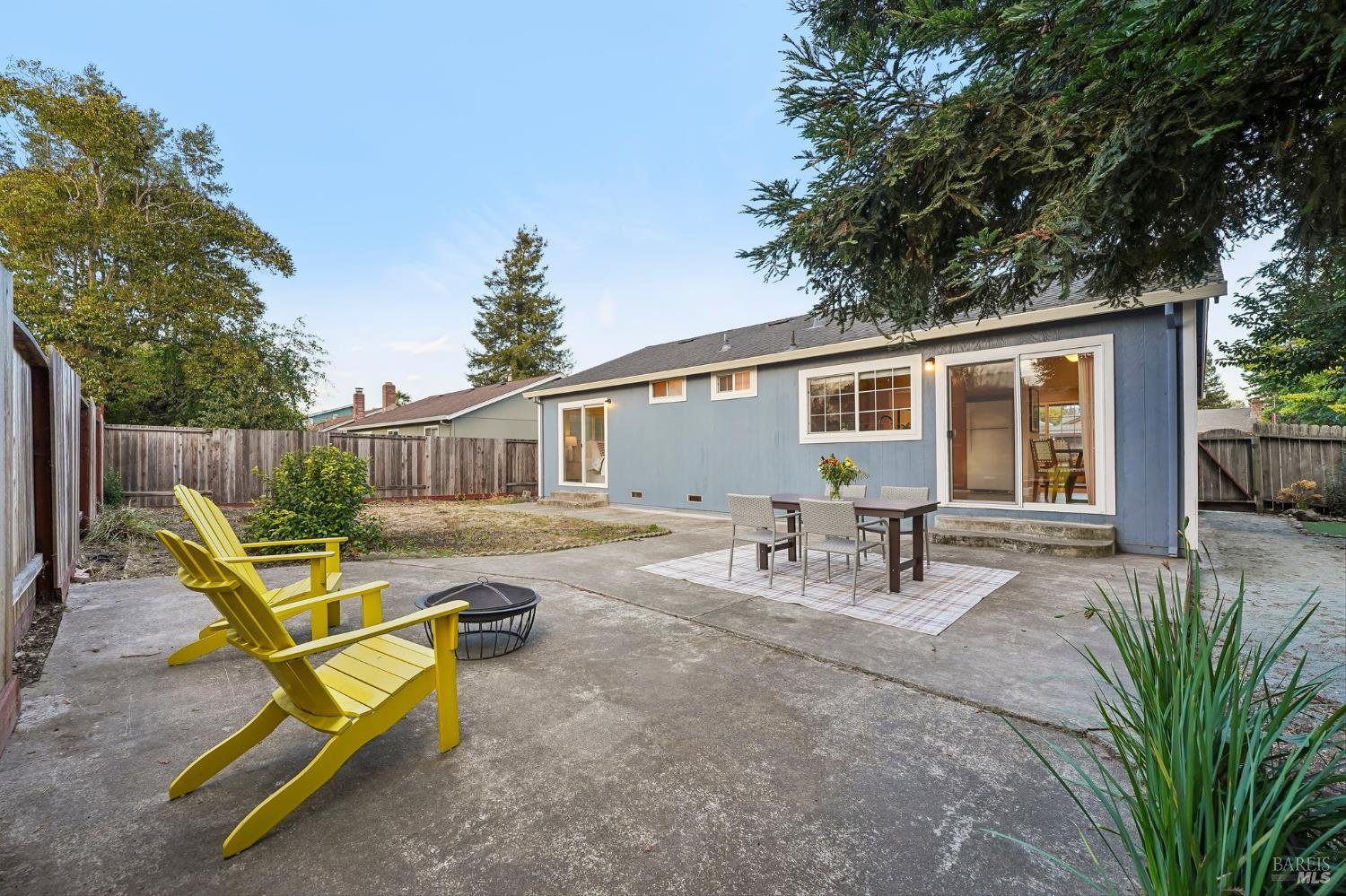 Backyard patio with yellow Adirondack chairs and a dining set beside the blue house.