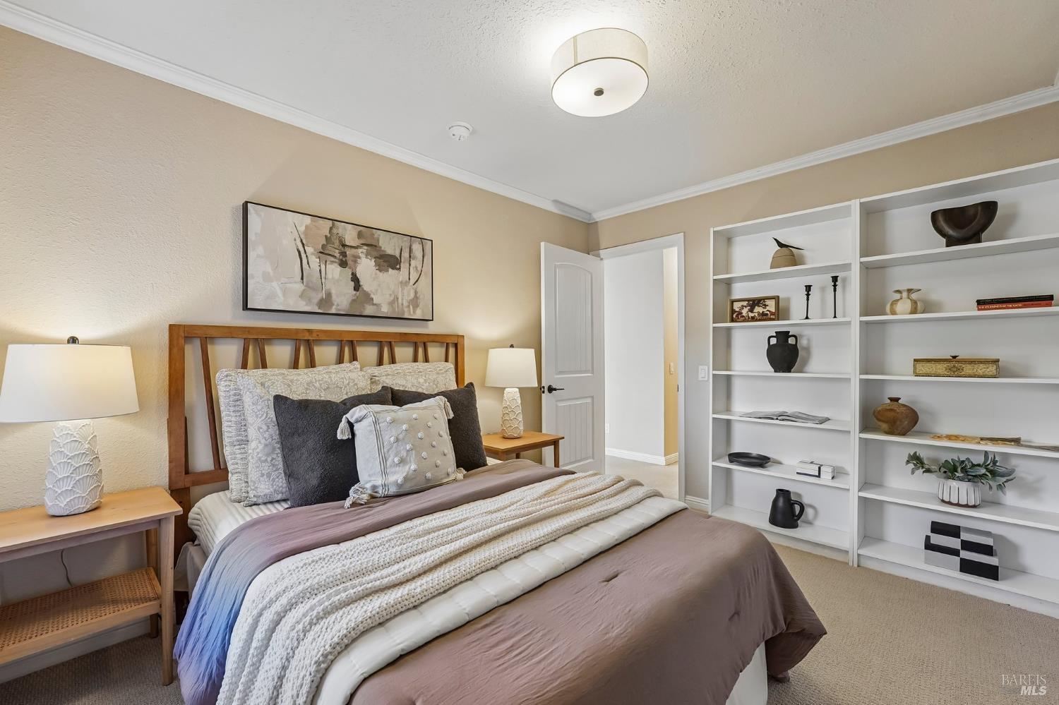 Staged bedroom with layered neutral bedding, wooden bed frame, and built-in white display shelves.