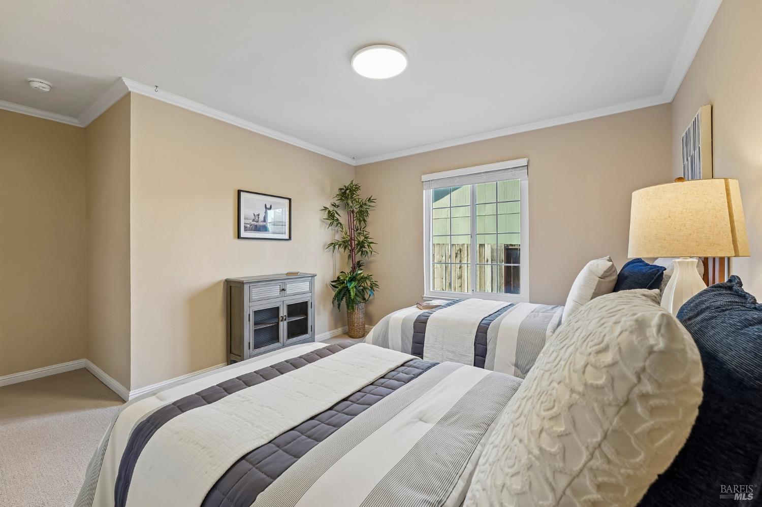 Staged bedroom with two beds, striped bedding, and a window overlooking a wooden fence.