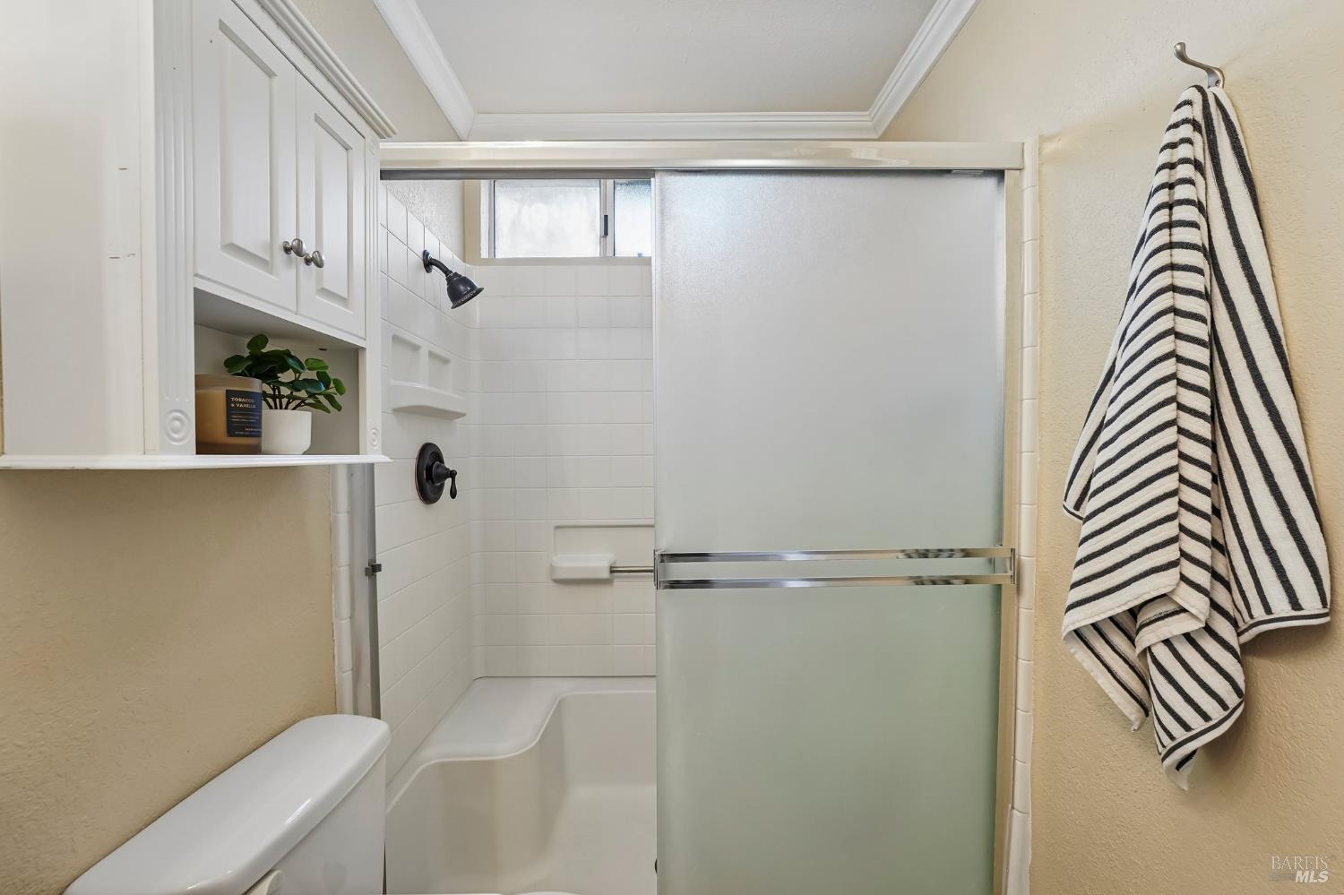 Bathroom with a white tub, frosted sliding shower door, built-in cabinetry, and striped towels.