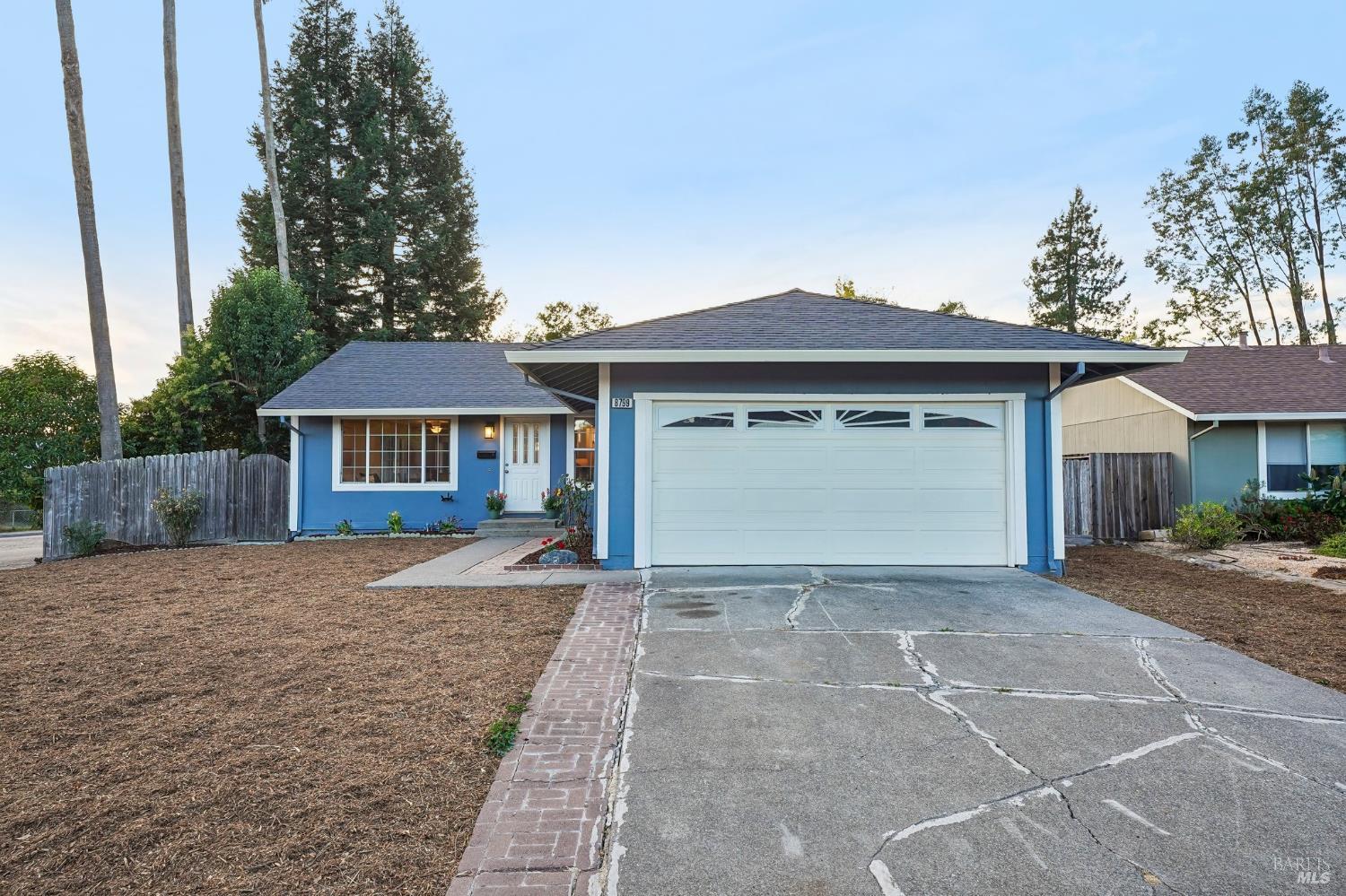 Blue single-story home with a white double garage and broad concrete driveway.