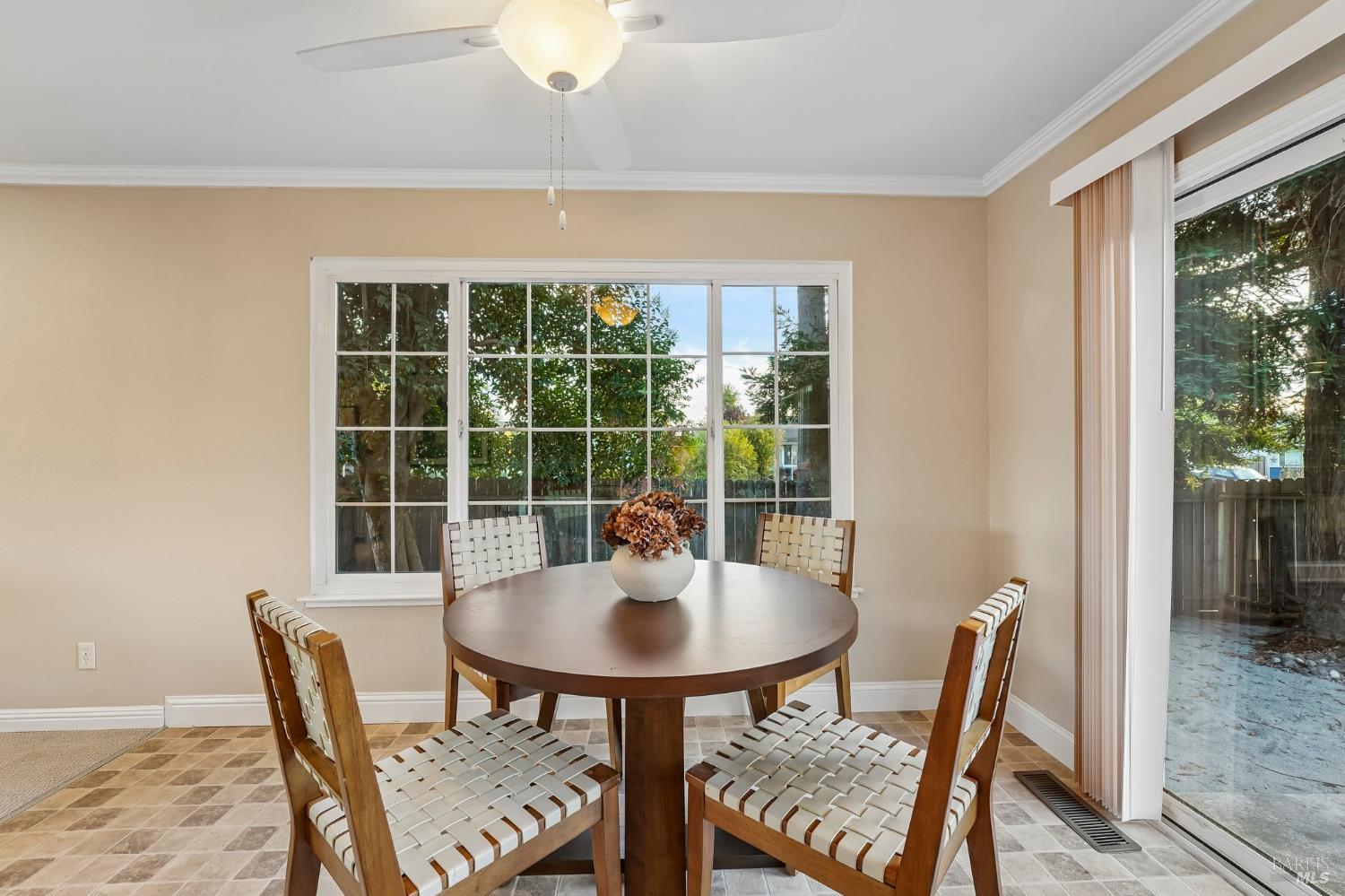 Dining room with a round wooden table, woven chairs, and large windows overlooking the yard.